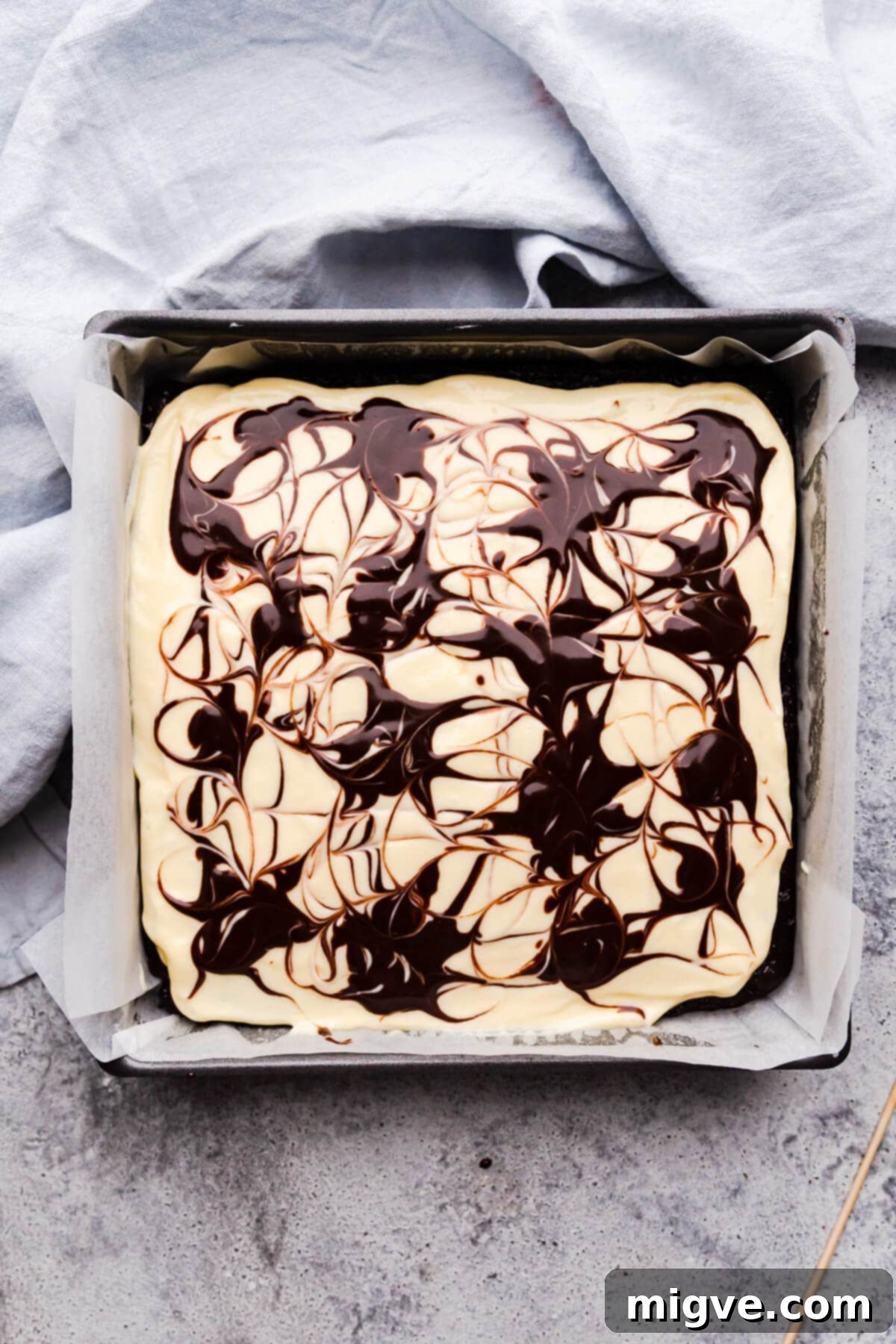 overhead view of square baking tin with cheesecake brownie batter inside