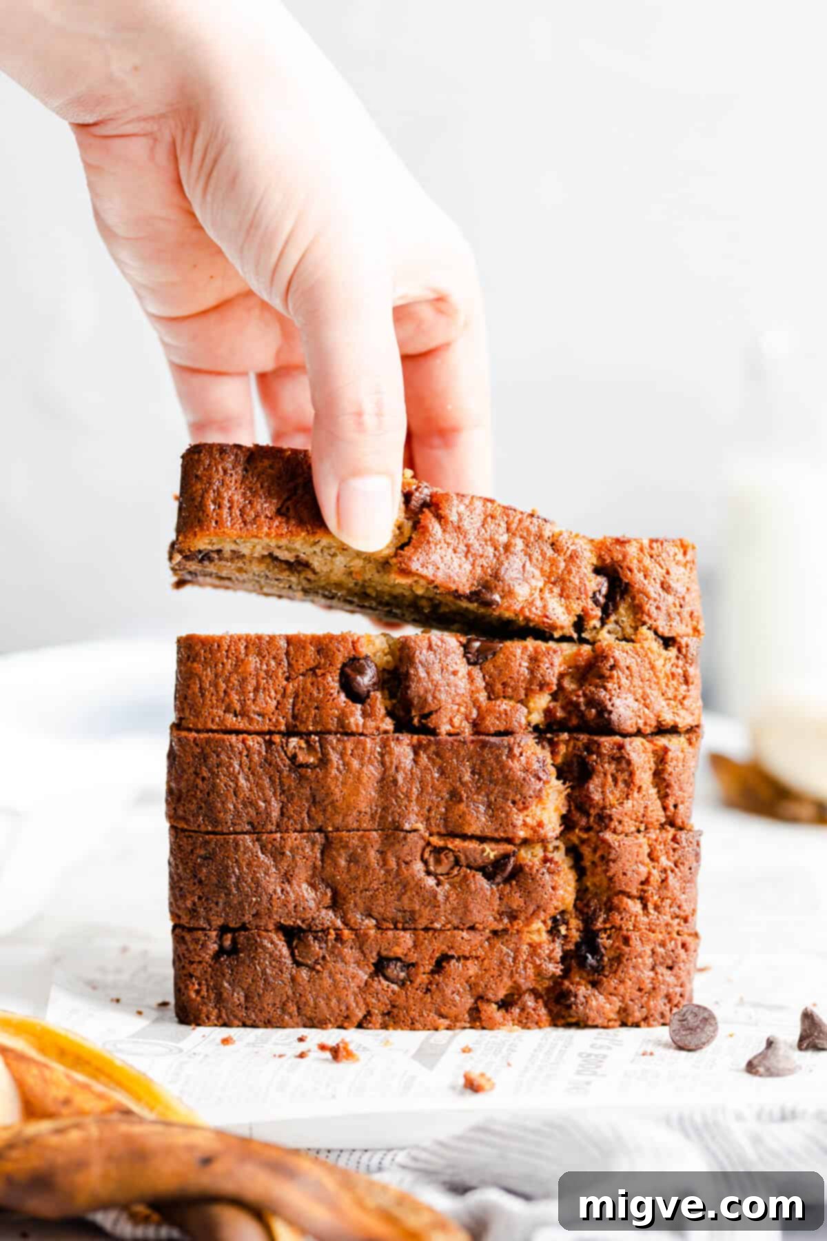 A hand reaching for a slice of moist chocolate chip banana bread from a stack of freshly baked slices, showcasing its tender texture.
