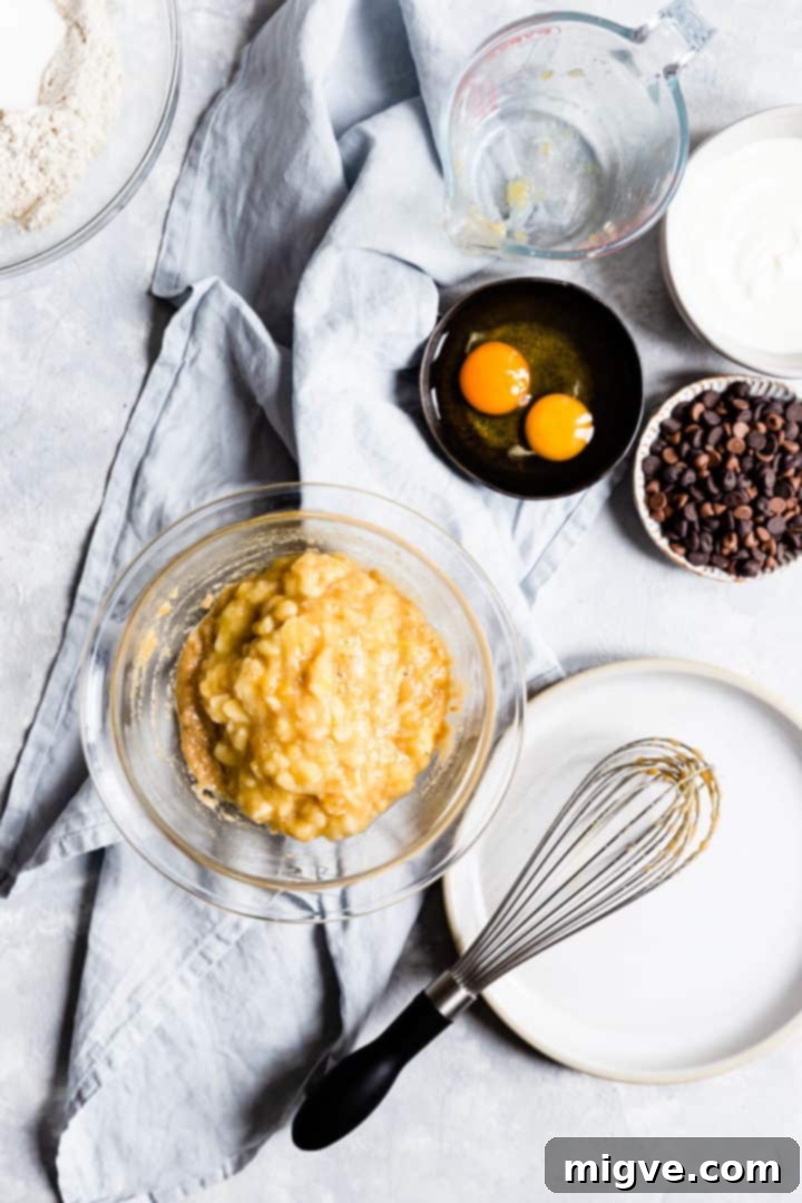 Top-down view of a clear glass bowl containing perfectly mashed ripe bananas, ready to be incorporated into the batter.