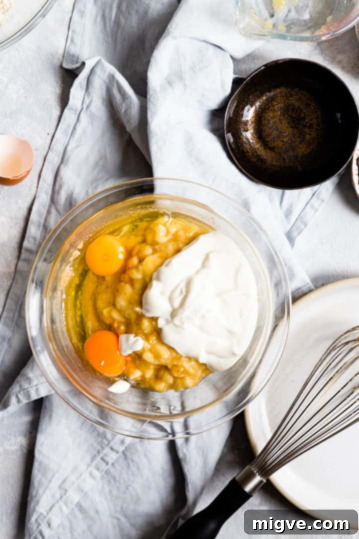 Overhead view of mashed bananas, creamy yogurt, and eggs in a mixing bowl, soon to be whisked into the batter.