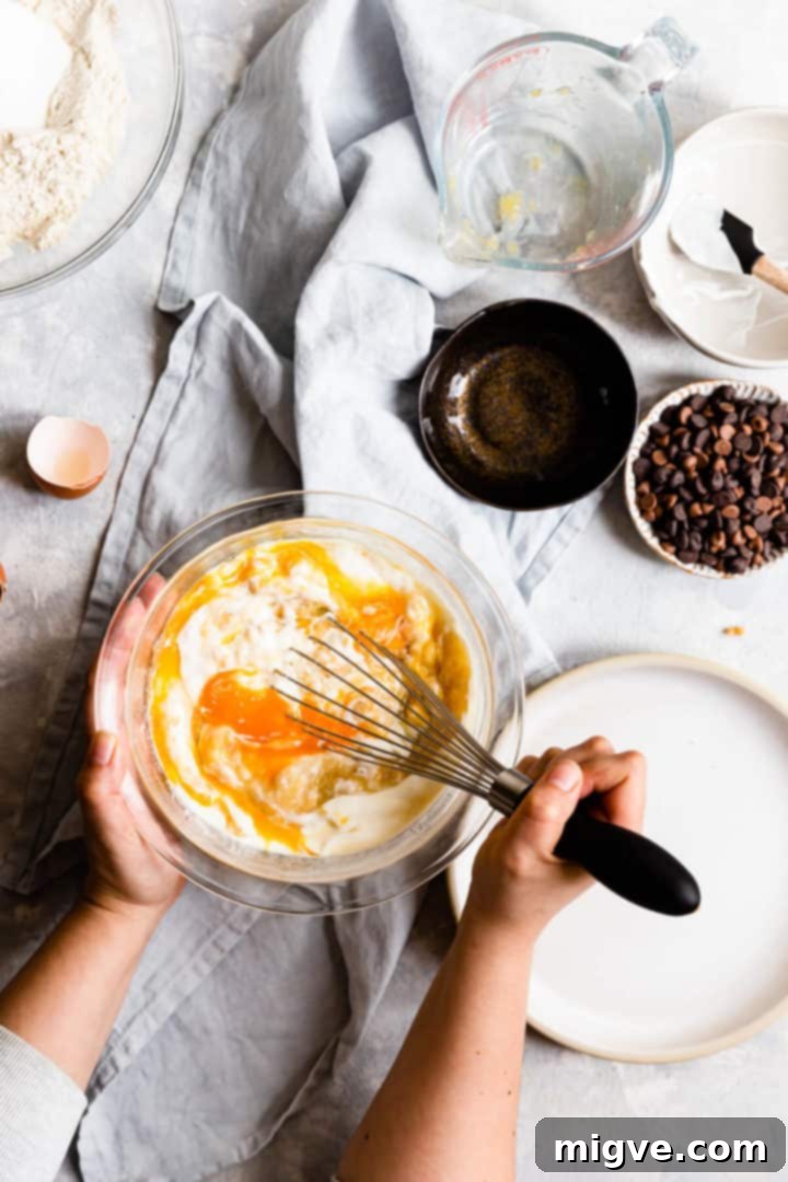 Overhead shot of a person gently whisking together the wet ingredients for chocolate chip banana bread in a large bowl, ensuring a smooth consistency.