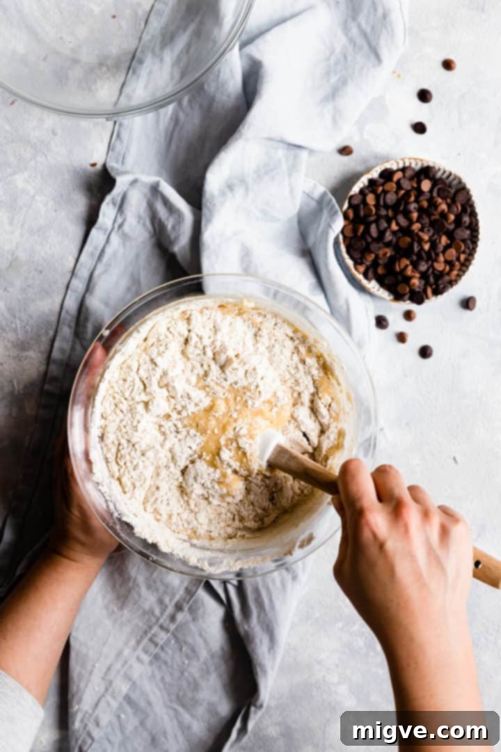 Overhead shot of a person carefully folding dry ingredients into the wet mixture with a rubber spatula, just until combined, to avoid overmixing.