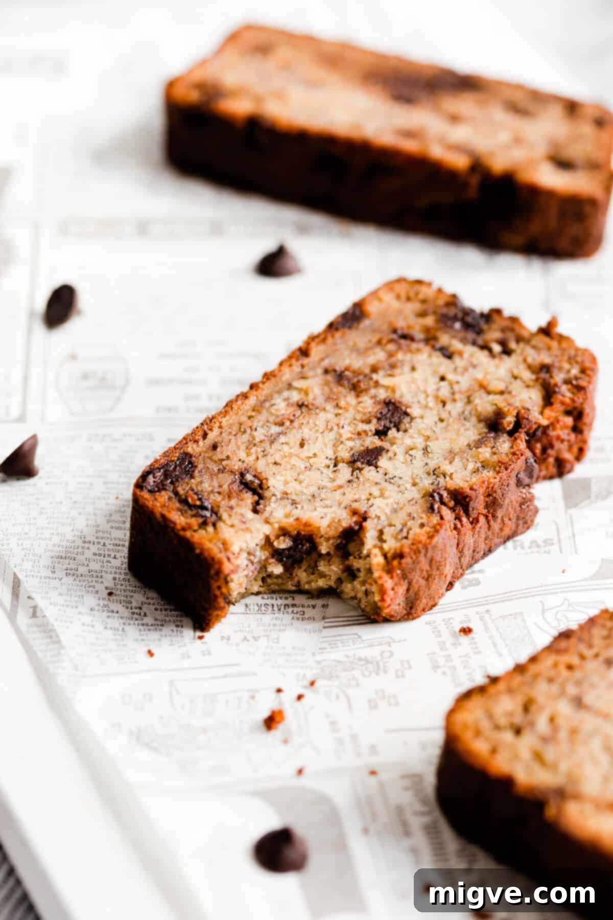 Close-up side view of a slice of chocolate chip banana bread, with a bite taken out, revealing its moist crumb and melted chocolate chips.