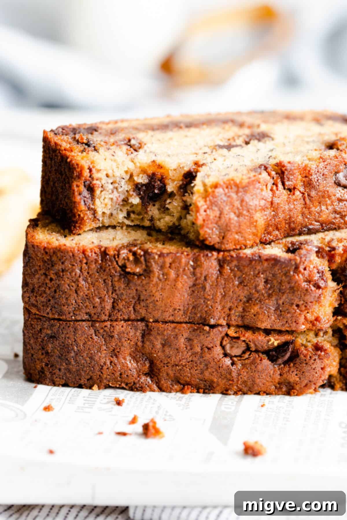 Side close-up of three thick slices of chocolate chip banana bread, perfectly stacked on top of each other, highlighting their height and rich texture.