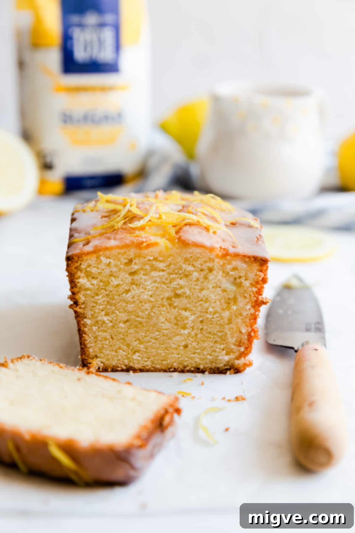 Zesty Small Batch Lemon Drizzle Cake 4 A close-up side view of a small-batch lemon drizzle cake loaf, with one slice elegantly cut off, revealing its moist, tender interior.