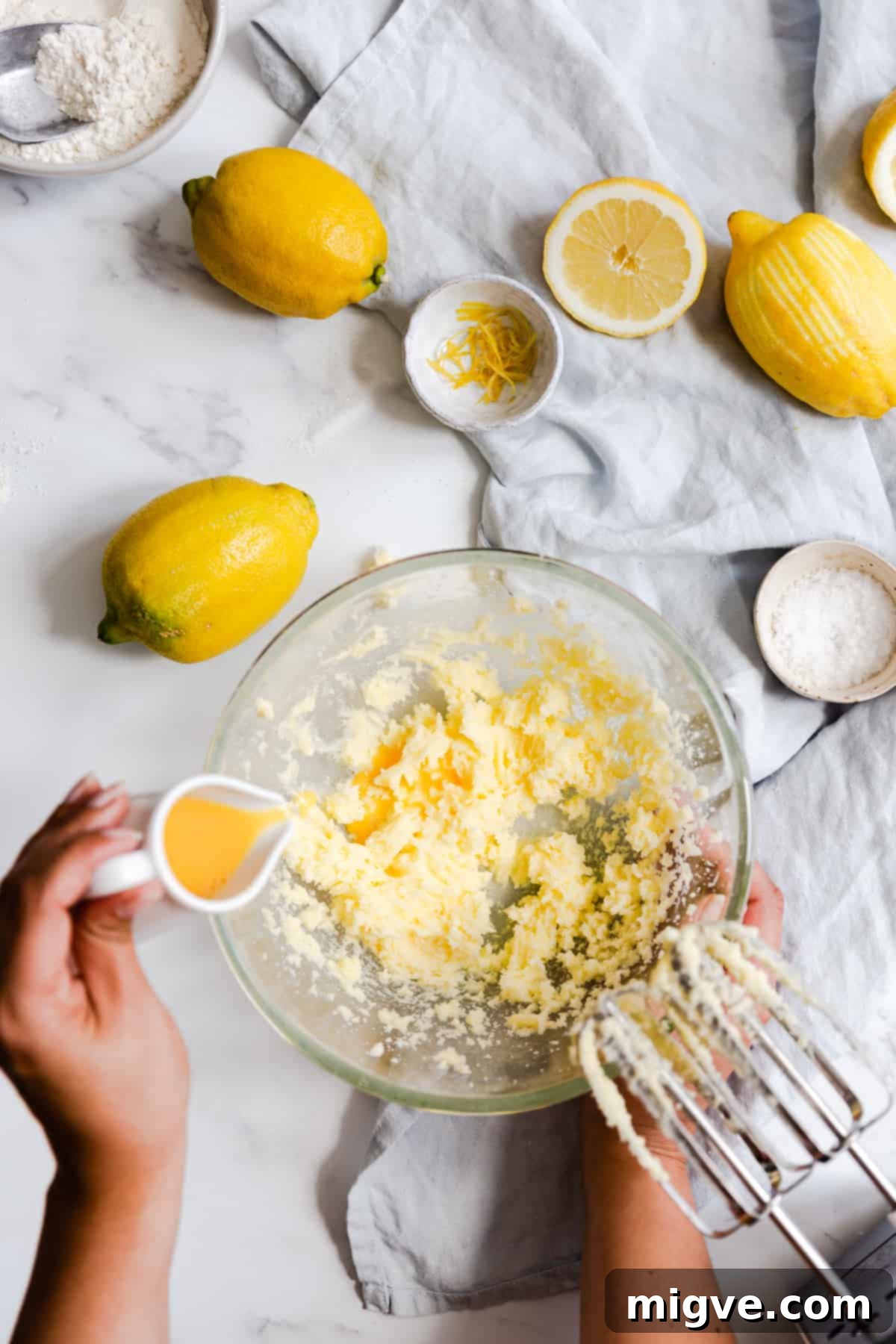 Zesty Small Batch Lemon Drizzle Cake 8 Top view of a hand adding beaten egg into a bowl of creamed butter and sugar, mixing gently.