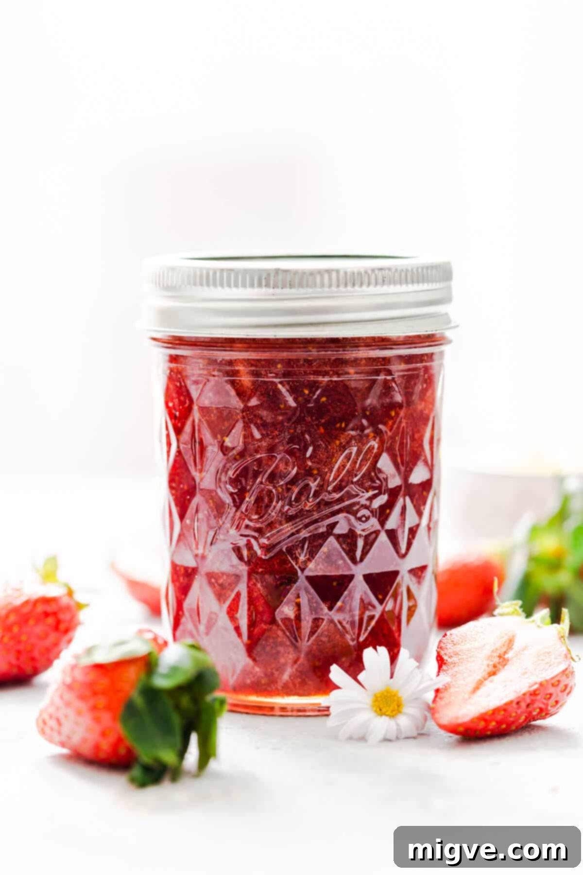 Effortless Strawberry Sunshine 11 straight ahead shot at a jar with strawberry jam and some strawberries around it