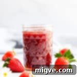 Effortless Strawberry Sunshine 14 straight ahead angle shot of a jar with strawberry jam and fresh strawberries on side