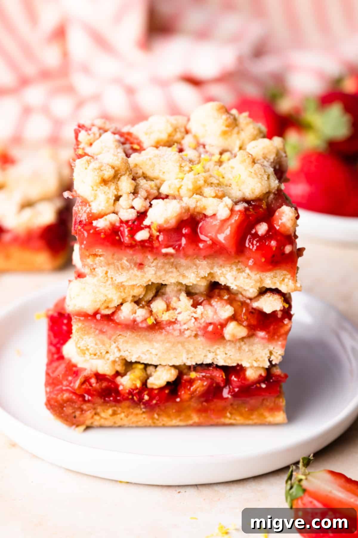 Three strawberry crumble bars stacked on top of each other on a small white plate, showcasing the layers of shortbread, strawberry filling, and oat crumble.