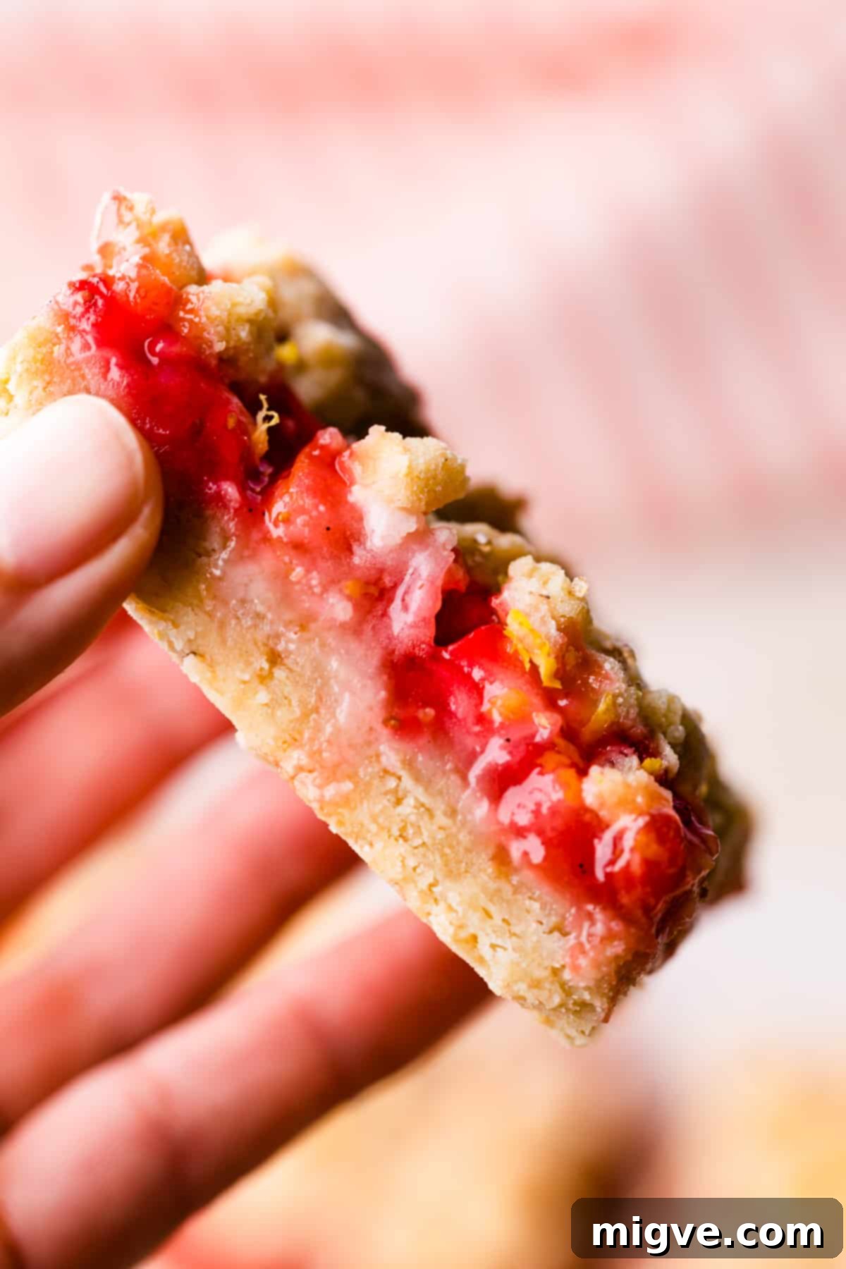 An individual slice of a strawberry crumble bar, perfectly baked with a golden topping, being held in a hand.