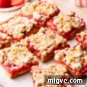 Slices of crumble bars with strawberries and crumble topping, lightly dusted with icing sugar and lemon zest.