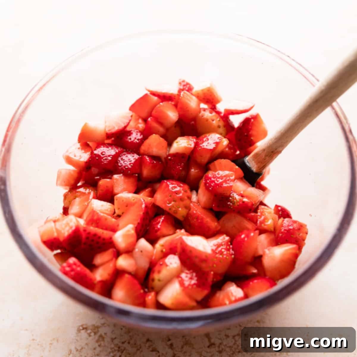 A glass bowl containing chopped strawberries and a small spatula, preparing for the filling.