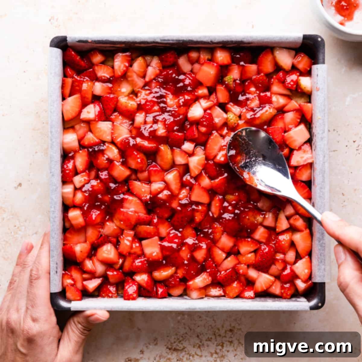 A baking tin with the pre-baked crumble base, now topped with an even layer of chopped strawberries, spread with a spoon.