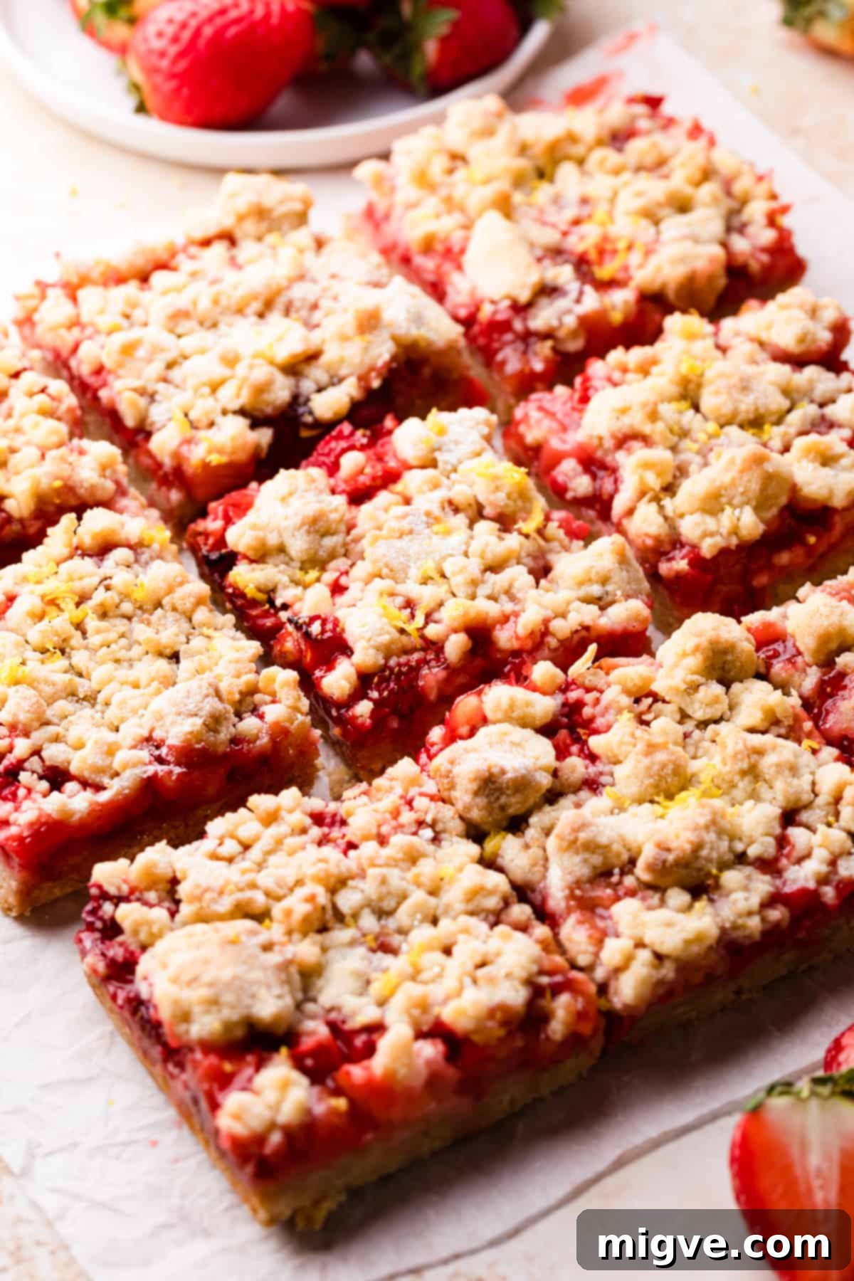 Baked strawberry crumble bars with streusel topping resting on a sheet of baking paper, just out of the oven.