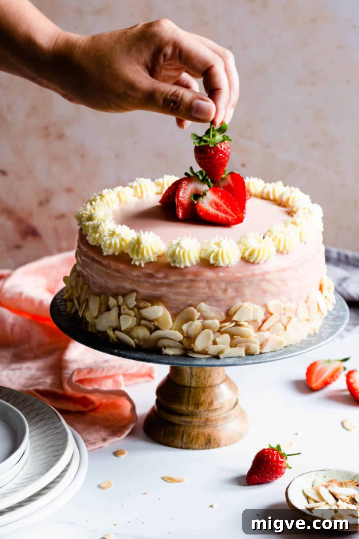 side shot of a hand lifting a strawberry from the top of the cake