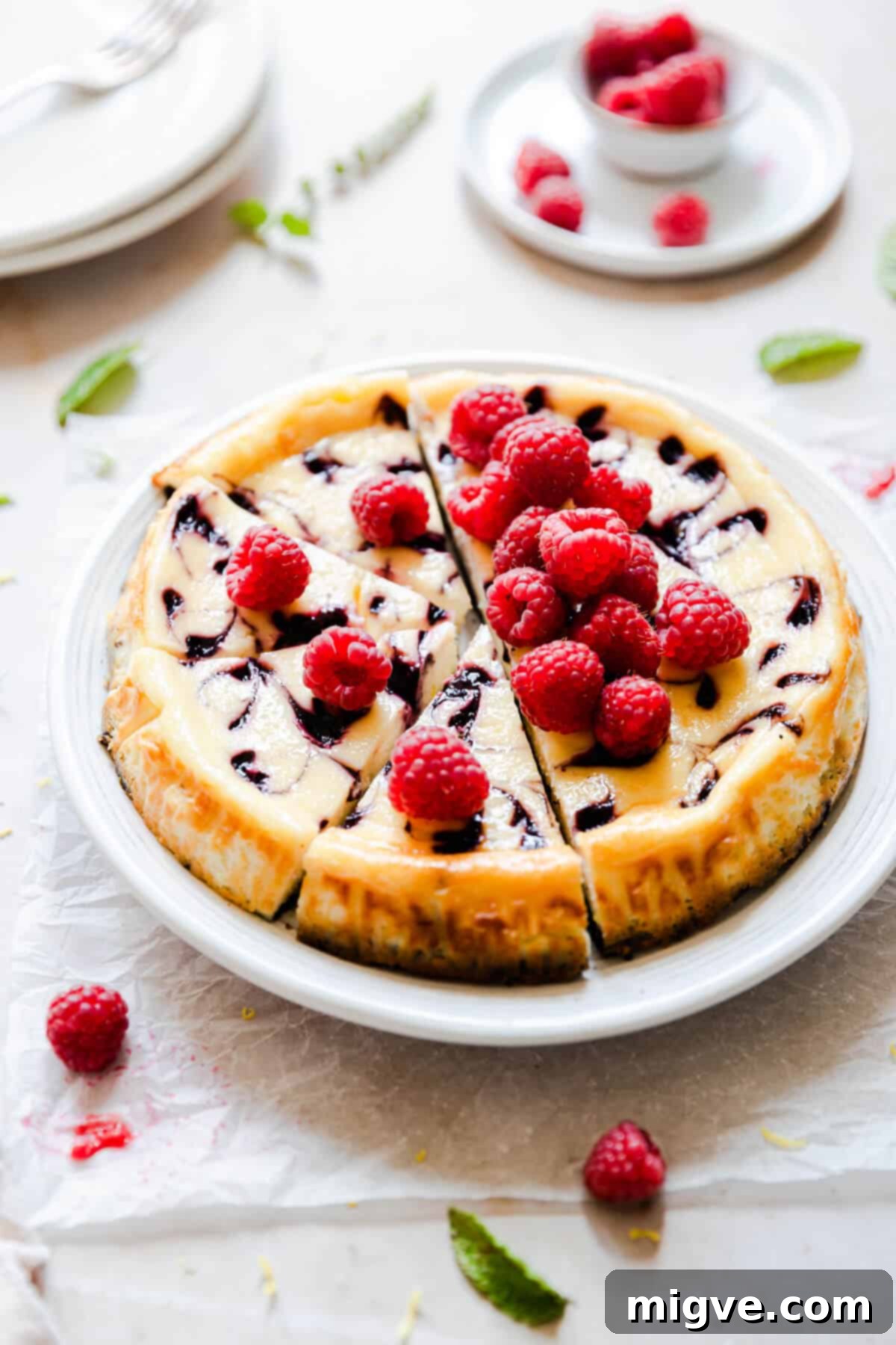 Side angle of a beautifully set raspberry ripple cheesecake, adorned with fresh raspberries and showing its swirled raspberry sauce.