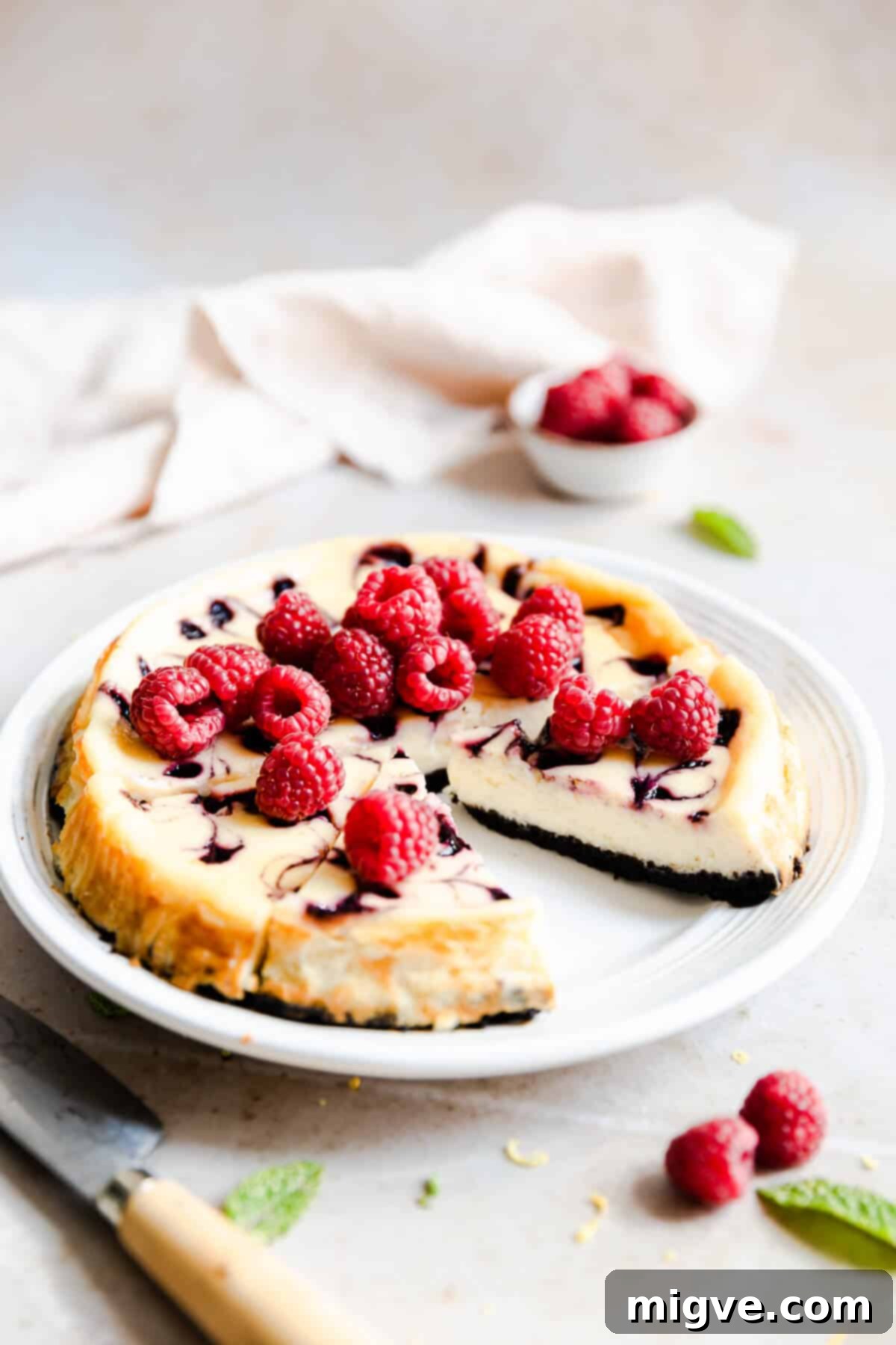Side angle of a delectable raspberry ripple cheesecake on a white plate, with a perfect slice already cut out and visible.