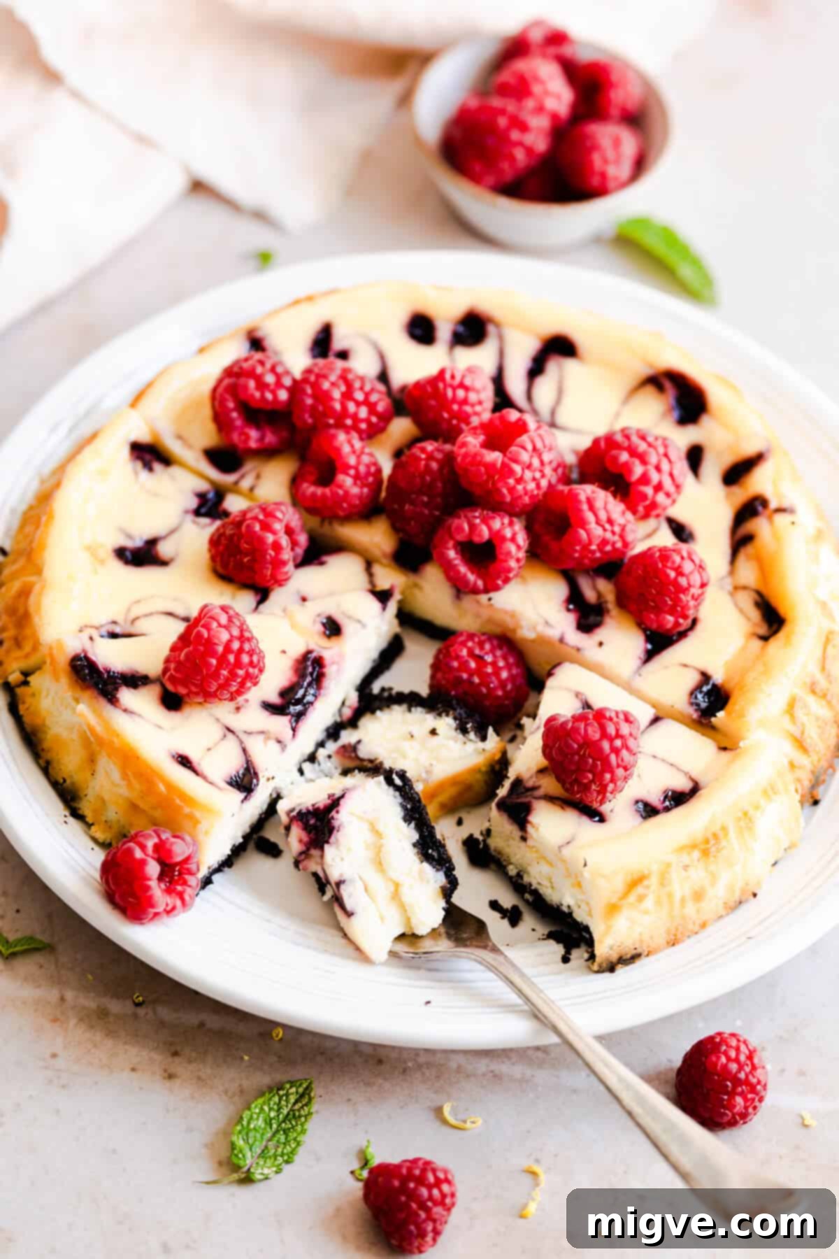 Close-up side view of a raspberry ripple cheesecake, with a fork gently taking out a piece to show its creamy interior.