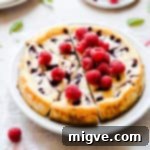 Side angle of a beautifully sliced raspberry ripple cheesecake topped with fresh raspberries and showing off the ripple effect.