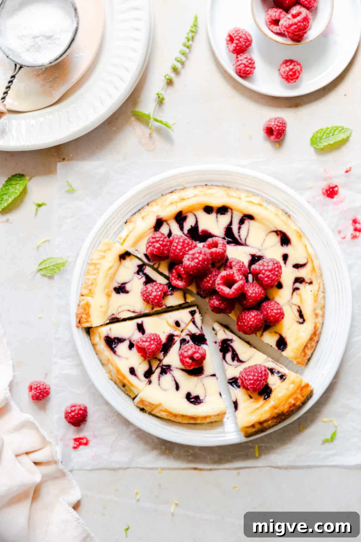 Top view of a beautifully swirled raspberry ripple cheesecake, garnished with fresh raspberries and the glistening raspberry sauce.