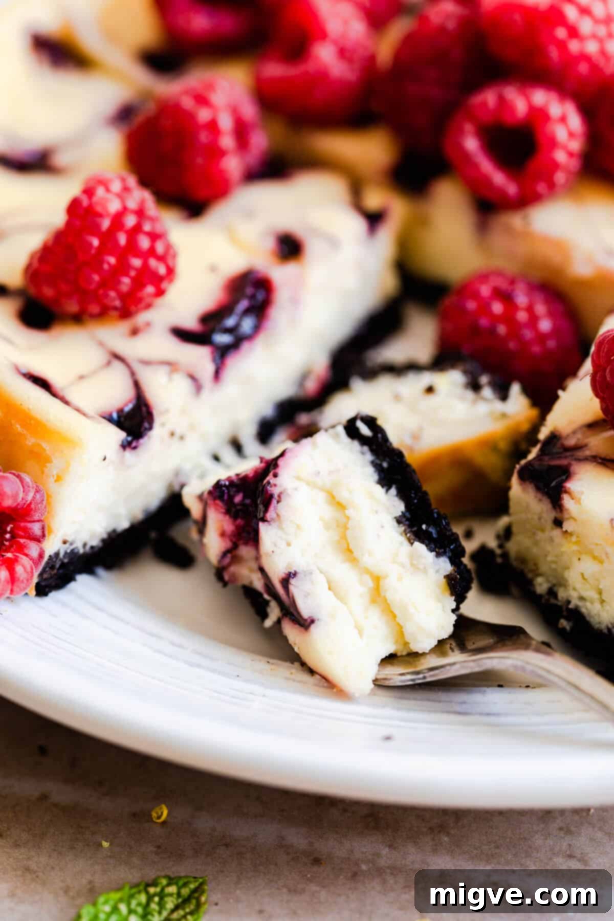 A super close-up shot of a perfect piece of raspberry ripple cheesecake on a fork, highlighting its creamy texture and raspberry swirls.
