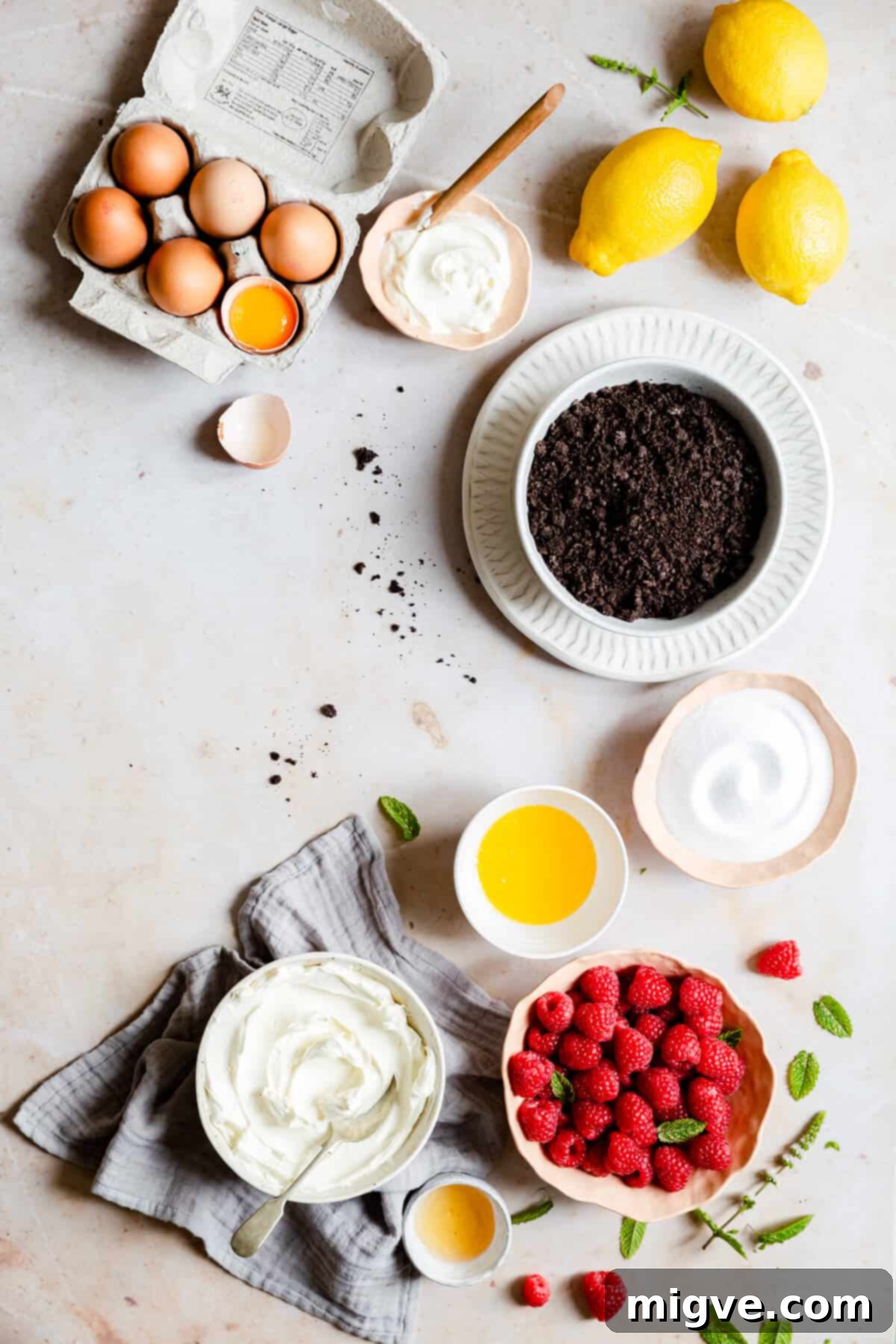Overhead shot of various bowls containing ingredients for raspberry cheesecake, all at room temperature and ready for mixing.