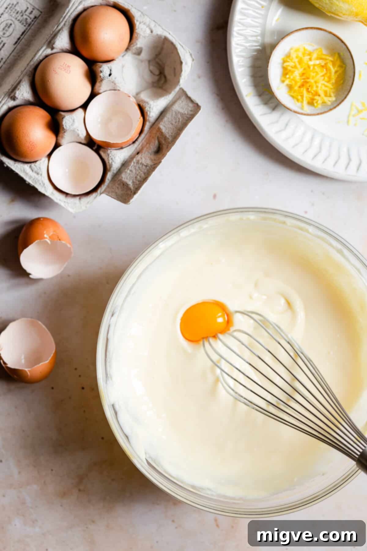 Overhead shot of a bowl with creamy cheesecake batter and an egg yolk being incorporated.