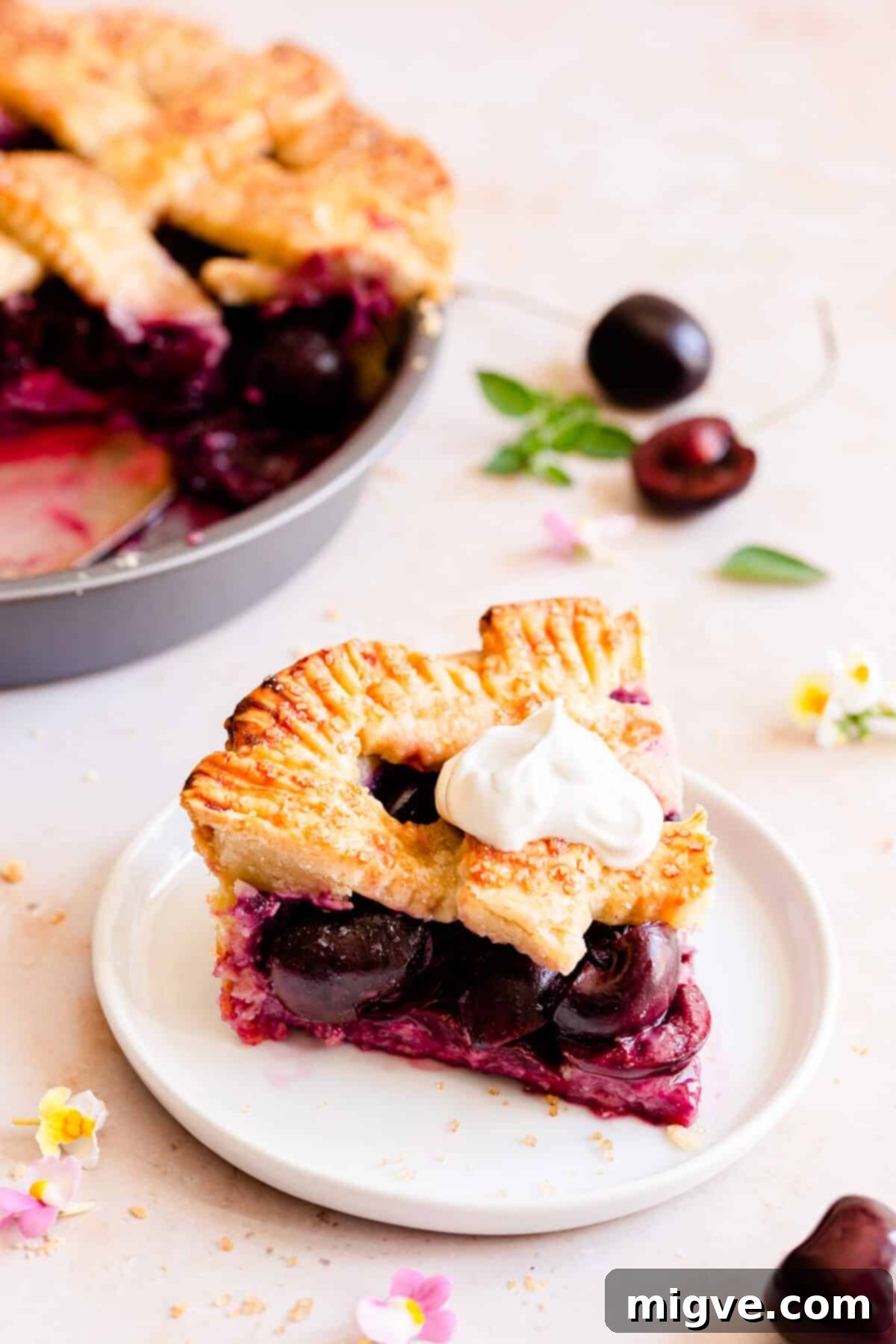 side close up at a slice of cherry pie topped with cream on a small plate