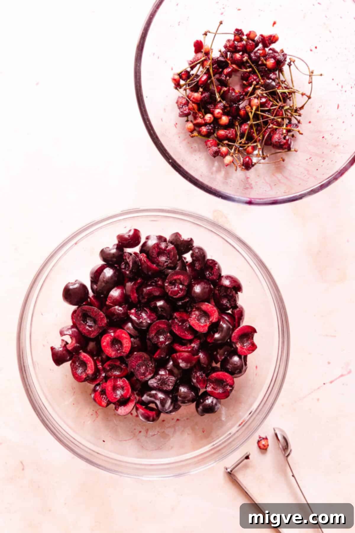 top view of pitted cherries in a bowl with another bowl of cherry stones and stalks