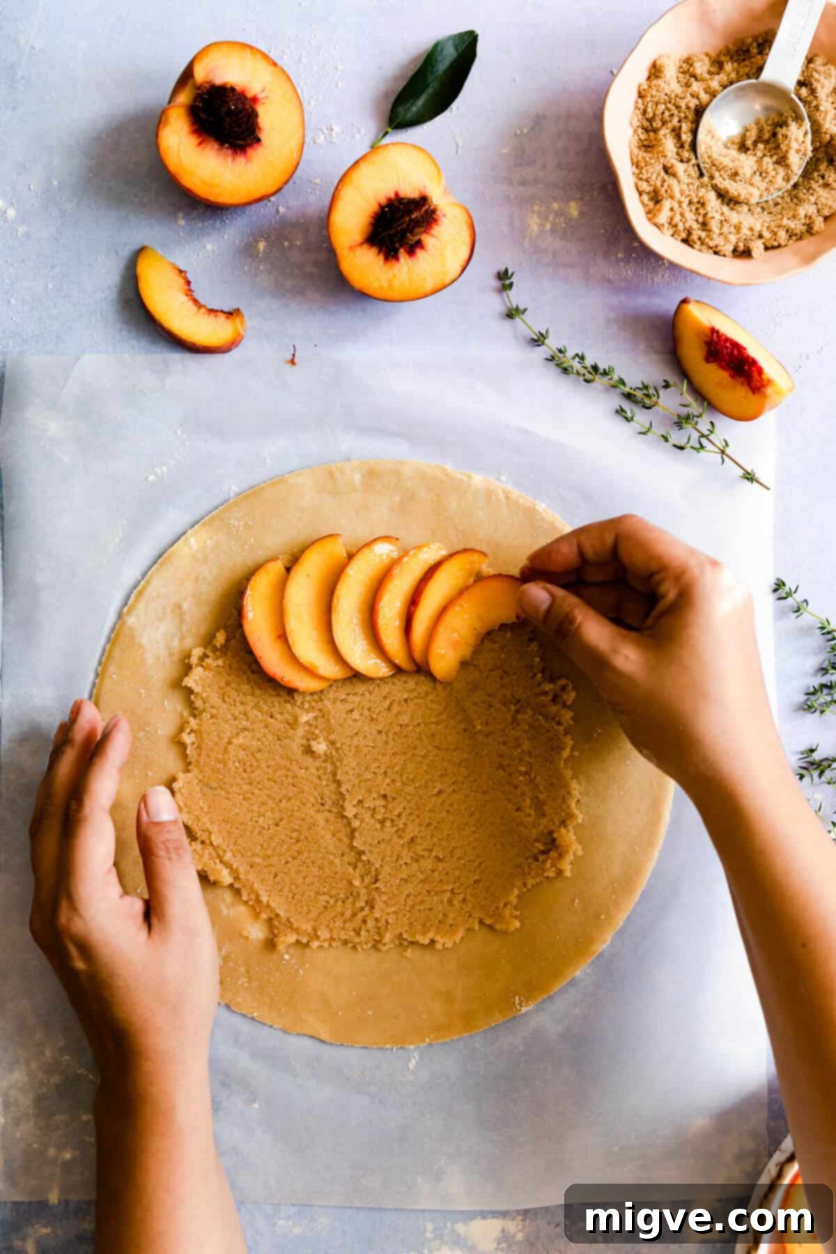 top view of perfectly sliced peaches being artfully arranged onto galette dough with frangipane