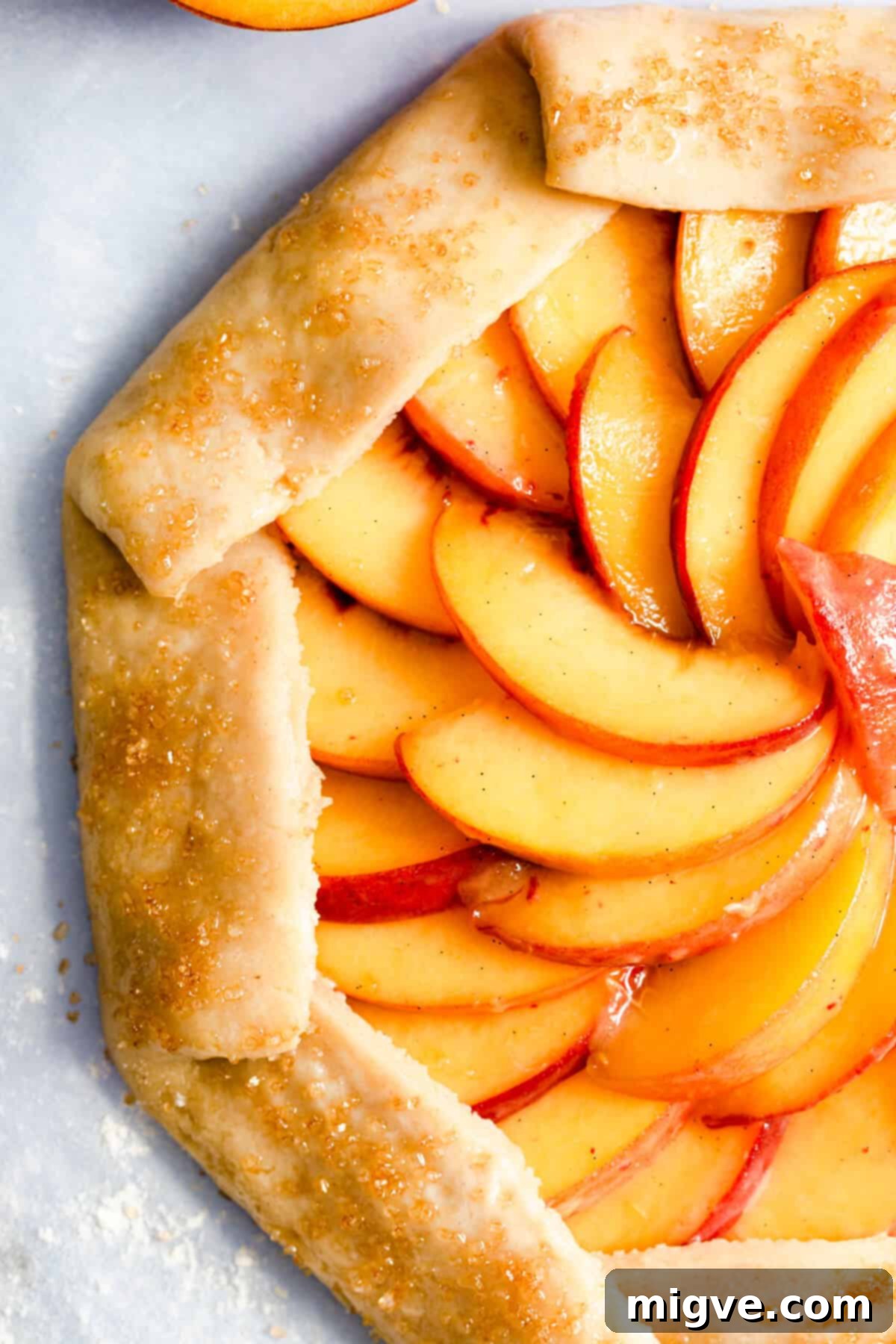 top view super close up of unbaked peach galette, showing fruit arrangement and sugar sprinkle