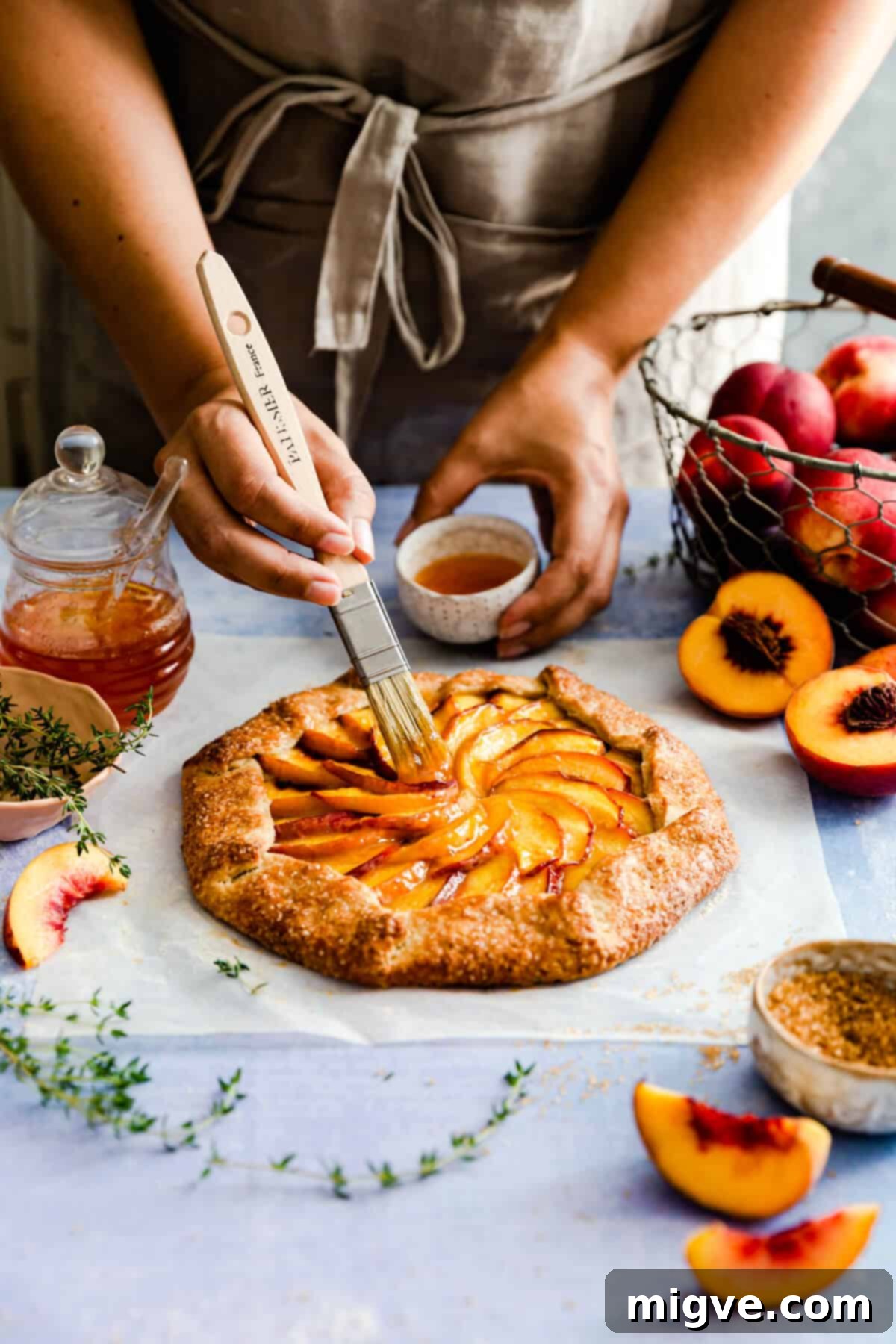 side view of person delicately brushing some jam on top of a baked peach galette