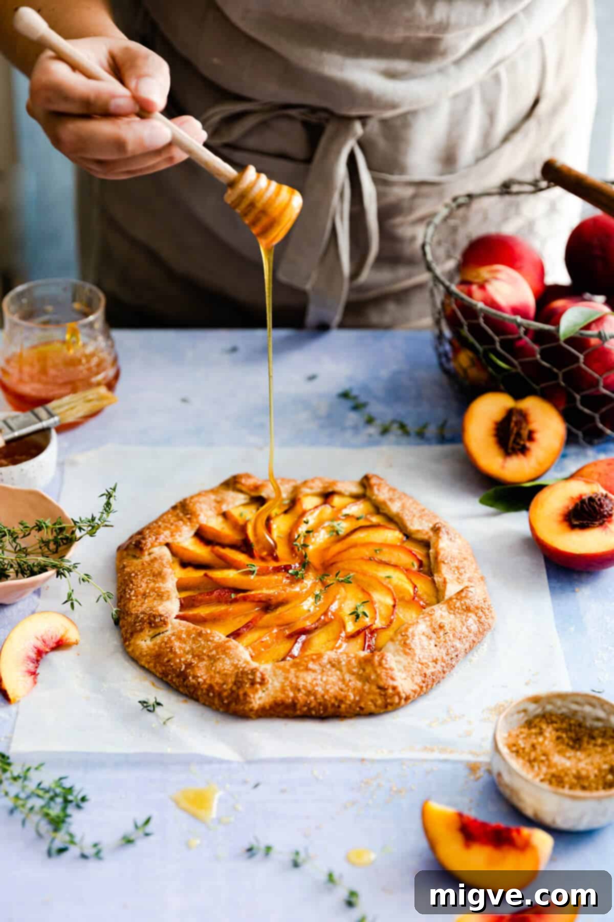 side angle showing a person drizzling fresh honey on a warm peach galette