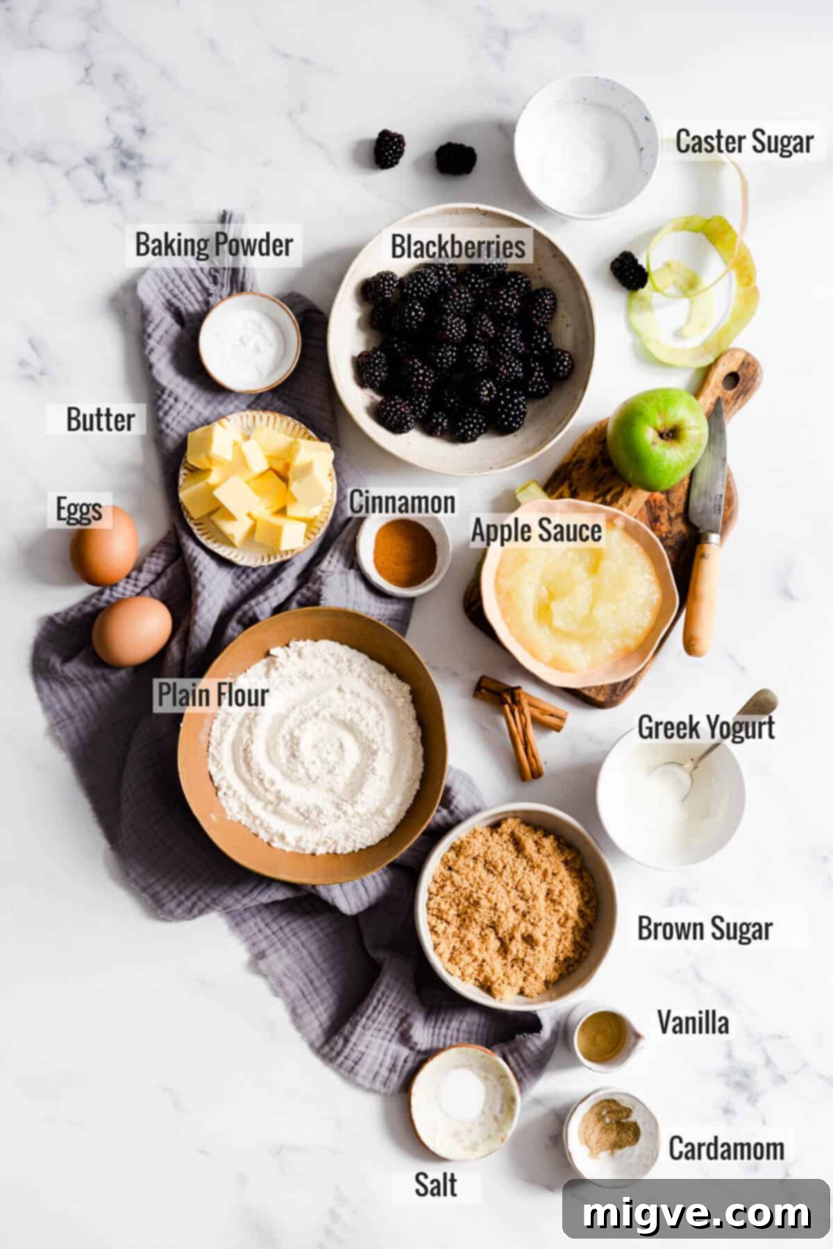 Overhead shot displaying all the fresh ingredients for spiced apple and blackberry cupcakes, including apples, blackberries, flour, sugar, and spices, laid out neatly.