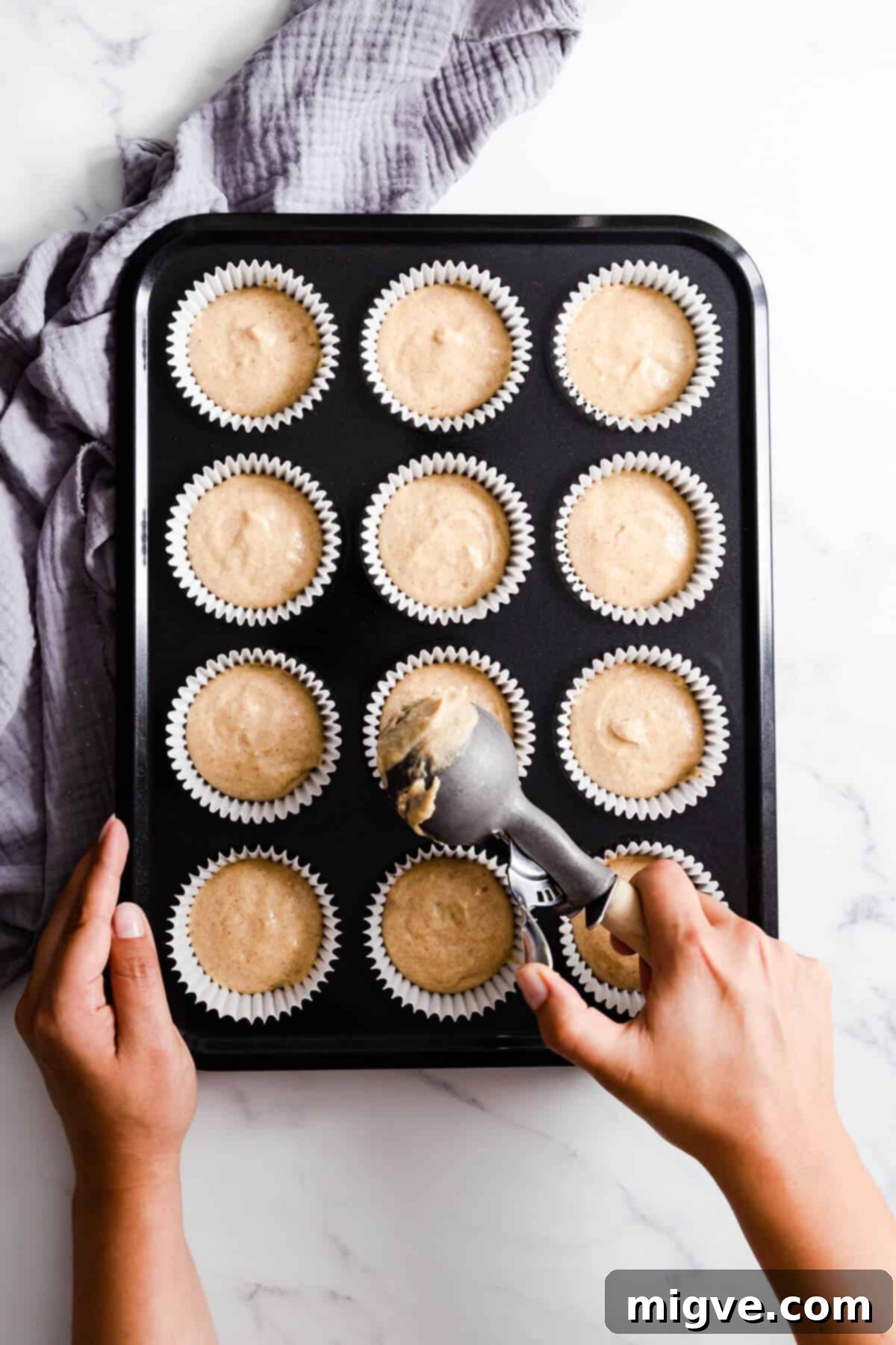 Top view of a baker carefully adding spiced apple cupcake batter into individual paper cases placed in a muffin tray.