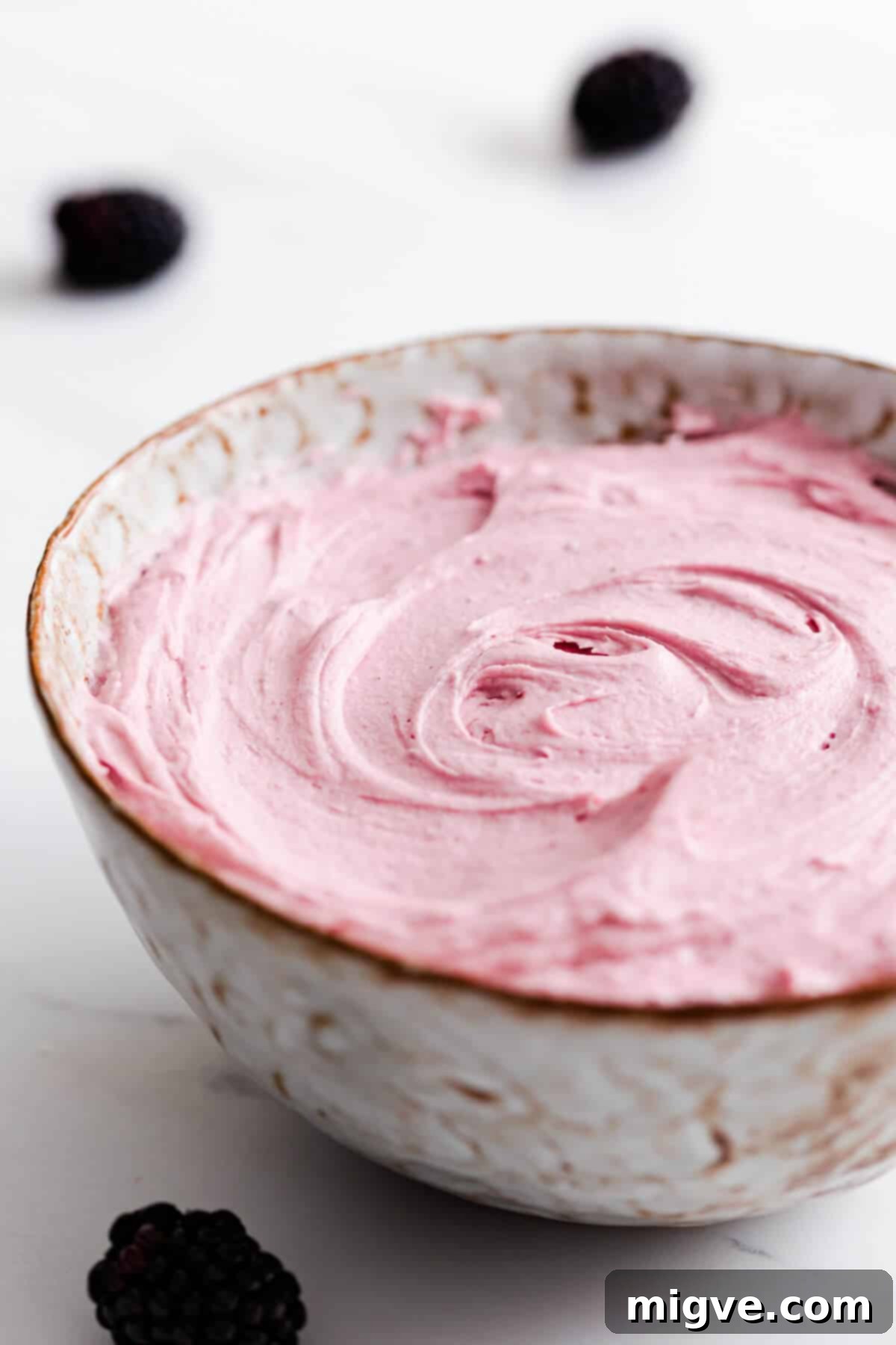 Side close-up of a large bowl filled with exquisitely smooth and vibrant pink blackberry buttercream, ready for piping.