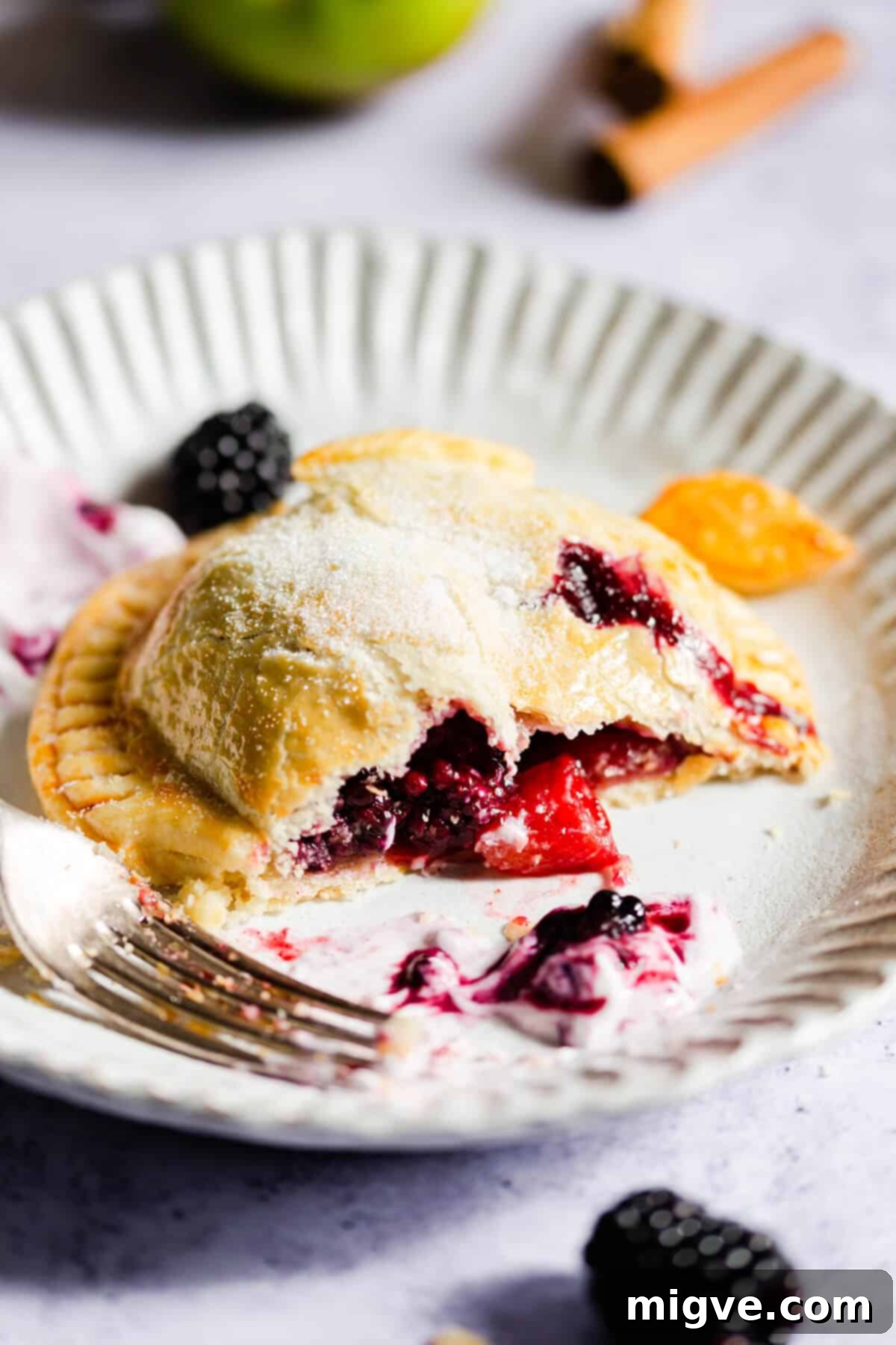side view of a hand pie on a plate, showing its filling of apples and blackberries
