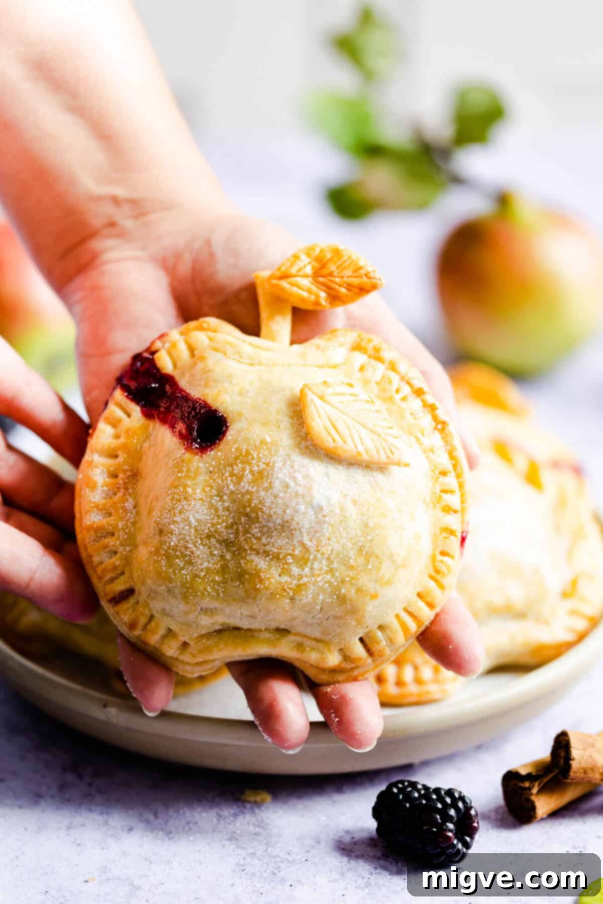 side close up of a person holding a pie shaped like an apple in palm of their hand