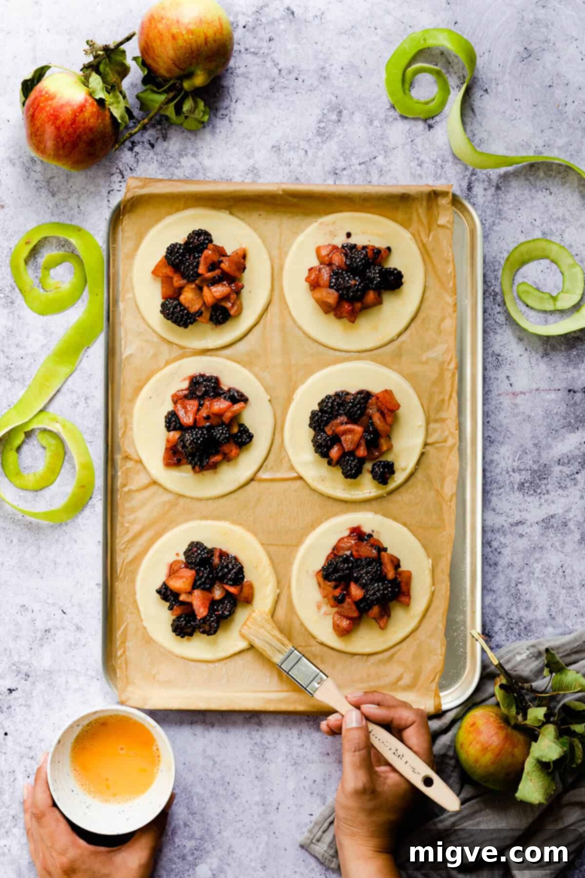 overhead shot of a person brushing an egg was around the edges of pastry circles