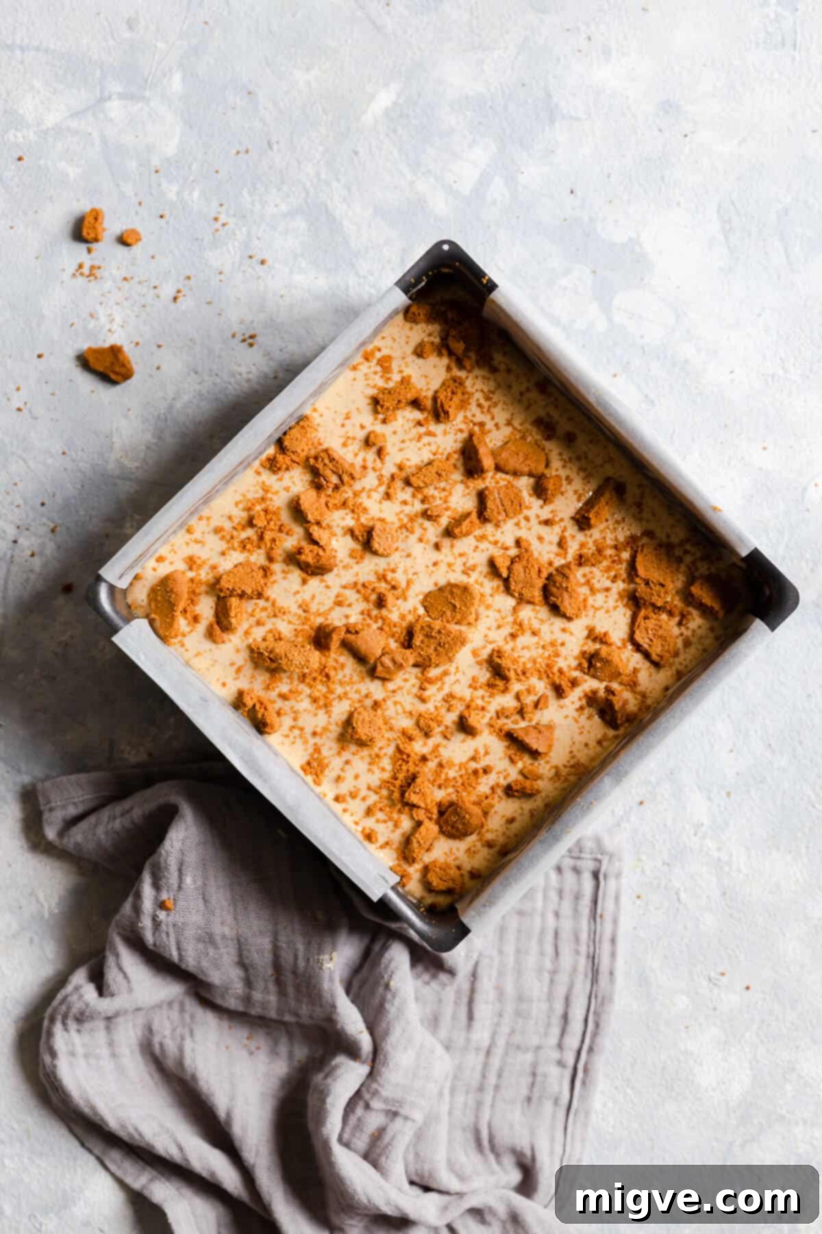 top view of cheesecake batter in a baking tin with crushed biscuits on top