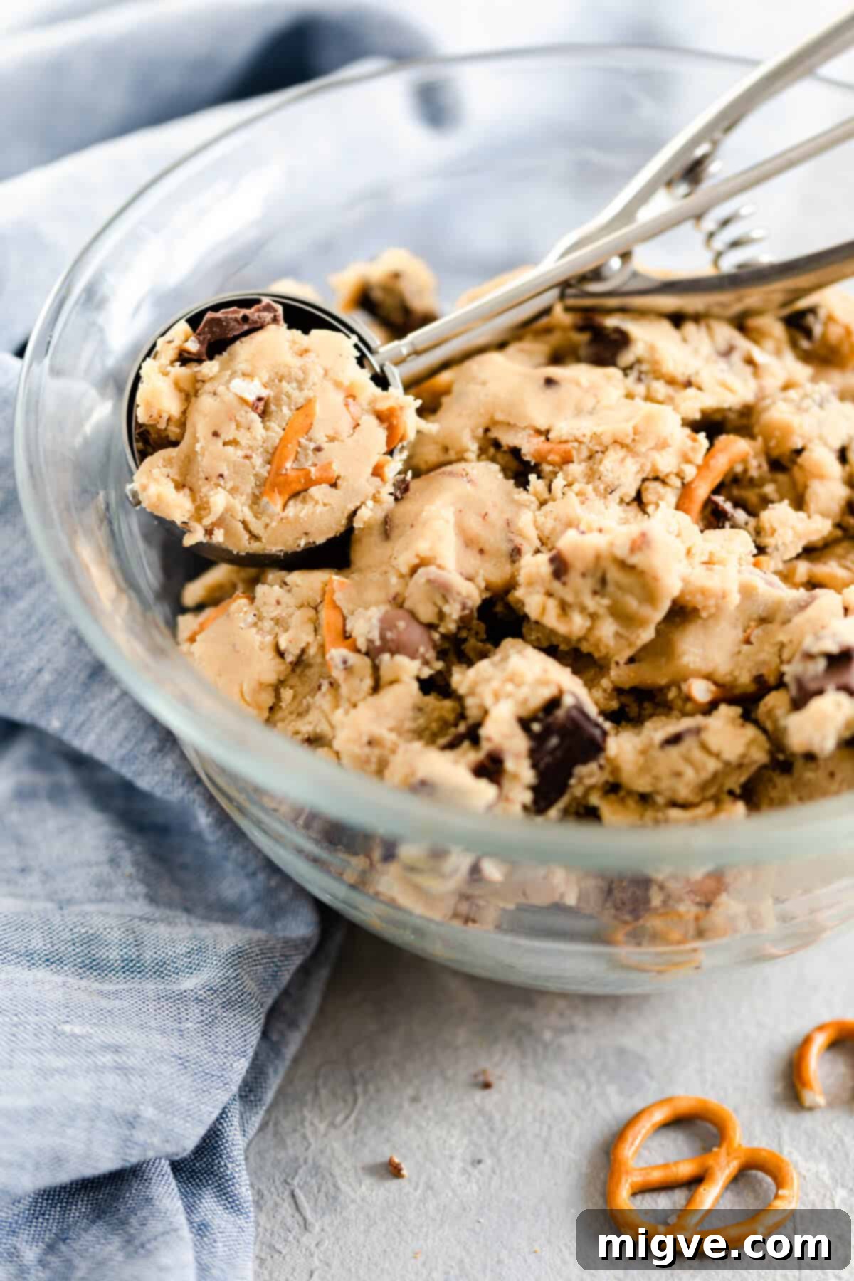 Side close-up of a glass mixing bowl filled with rich, unbaked cookie dough, speckled with chocolate chunks and pretzel pieces, ready for chilling.