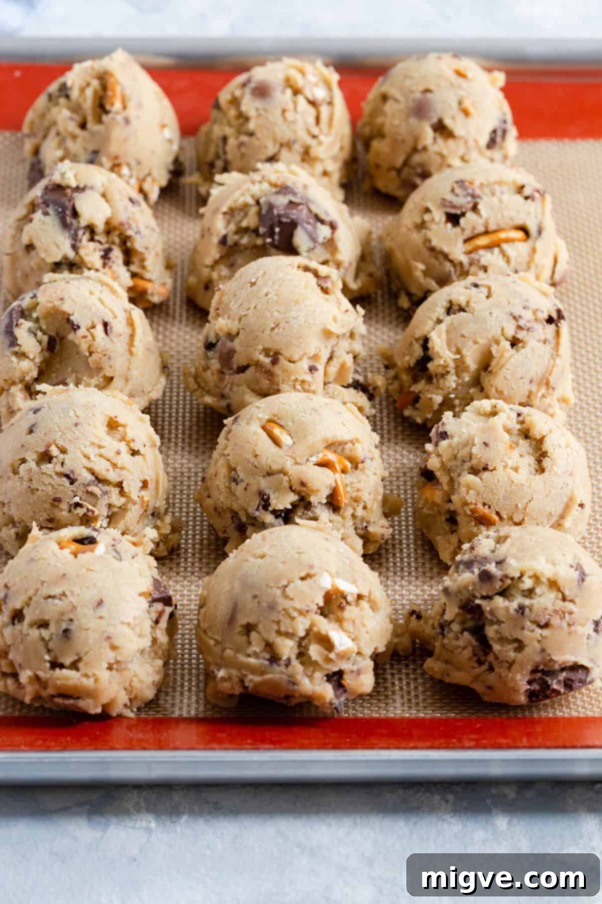 Side close-up of perfectly scooped balls of chocolate pretzel cookie dough arranged on a silicone baking mat, ready for chilling and baking.
