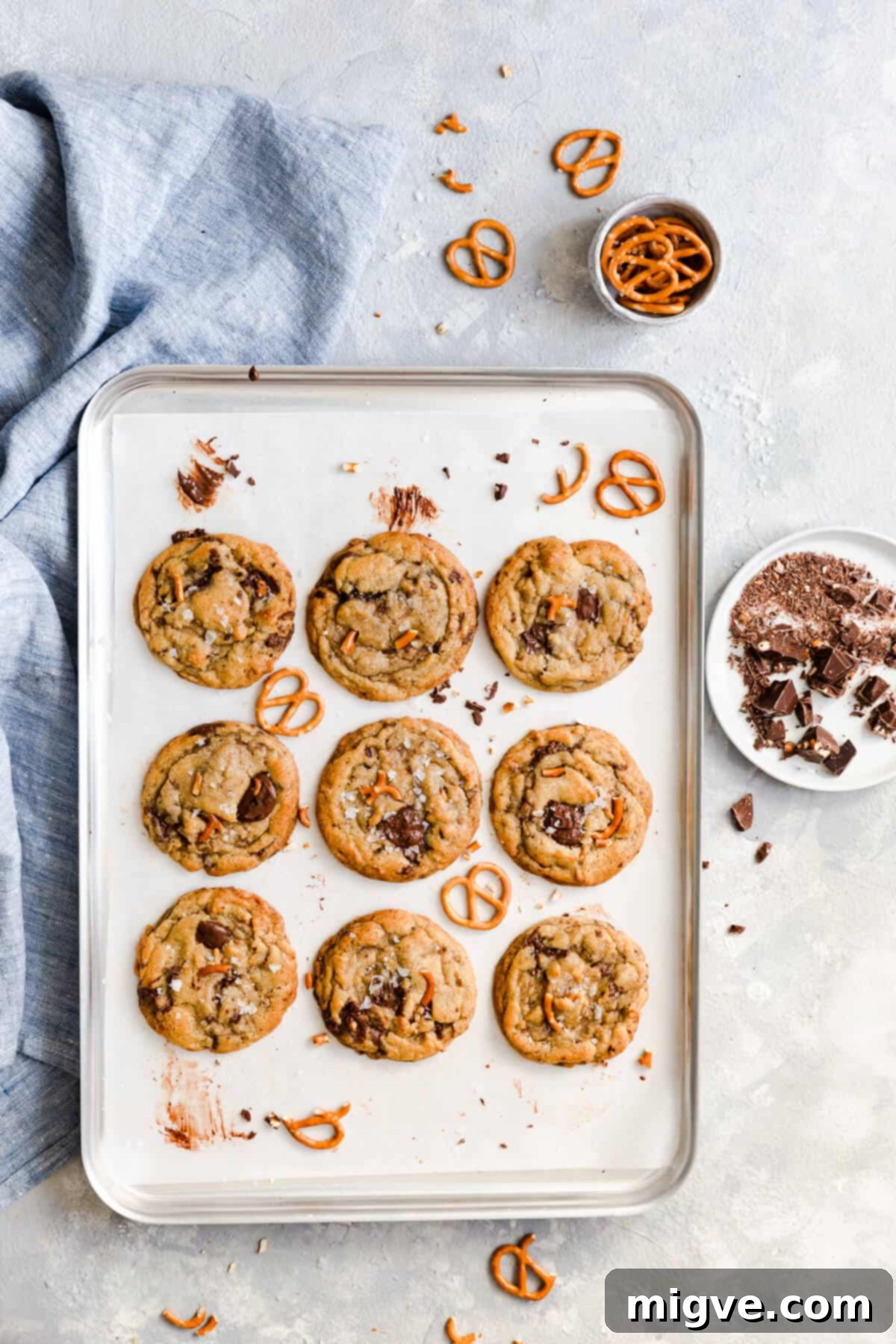 Overhead shot of a baking tray with nine golden-brown chocolate pretzel cookies, freshly baked and glistening.