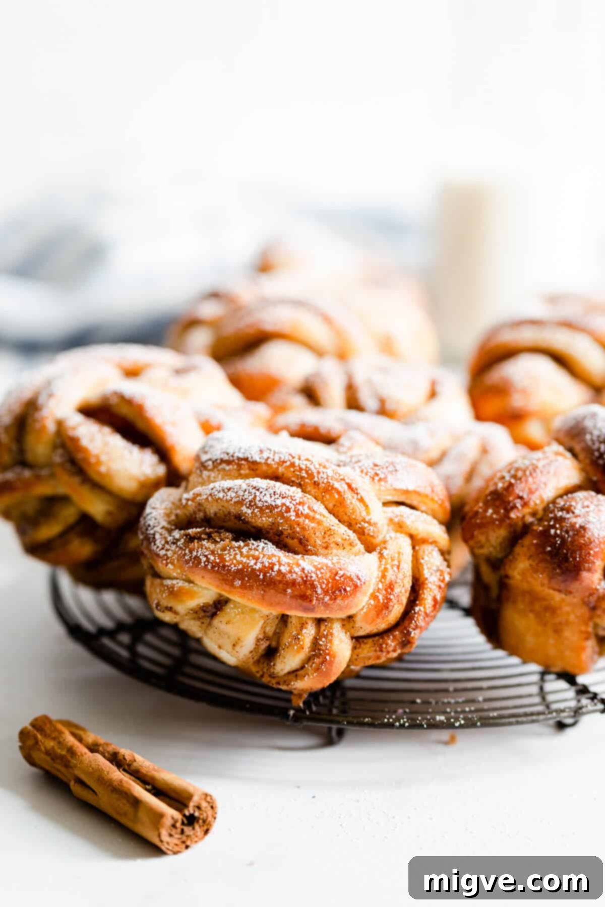 side shot of golden cinnamon rolls with icing sugar on a cooling rack