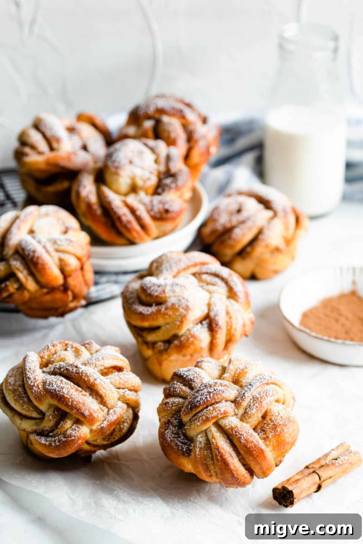 side angle shot of cinnamon buns with icing sugar and a bottle of milk in the background