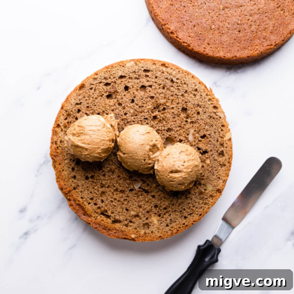 a round cake sponge with scoops of buttercream on top of it.