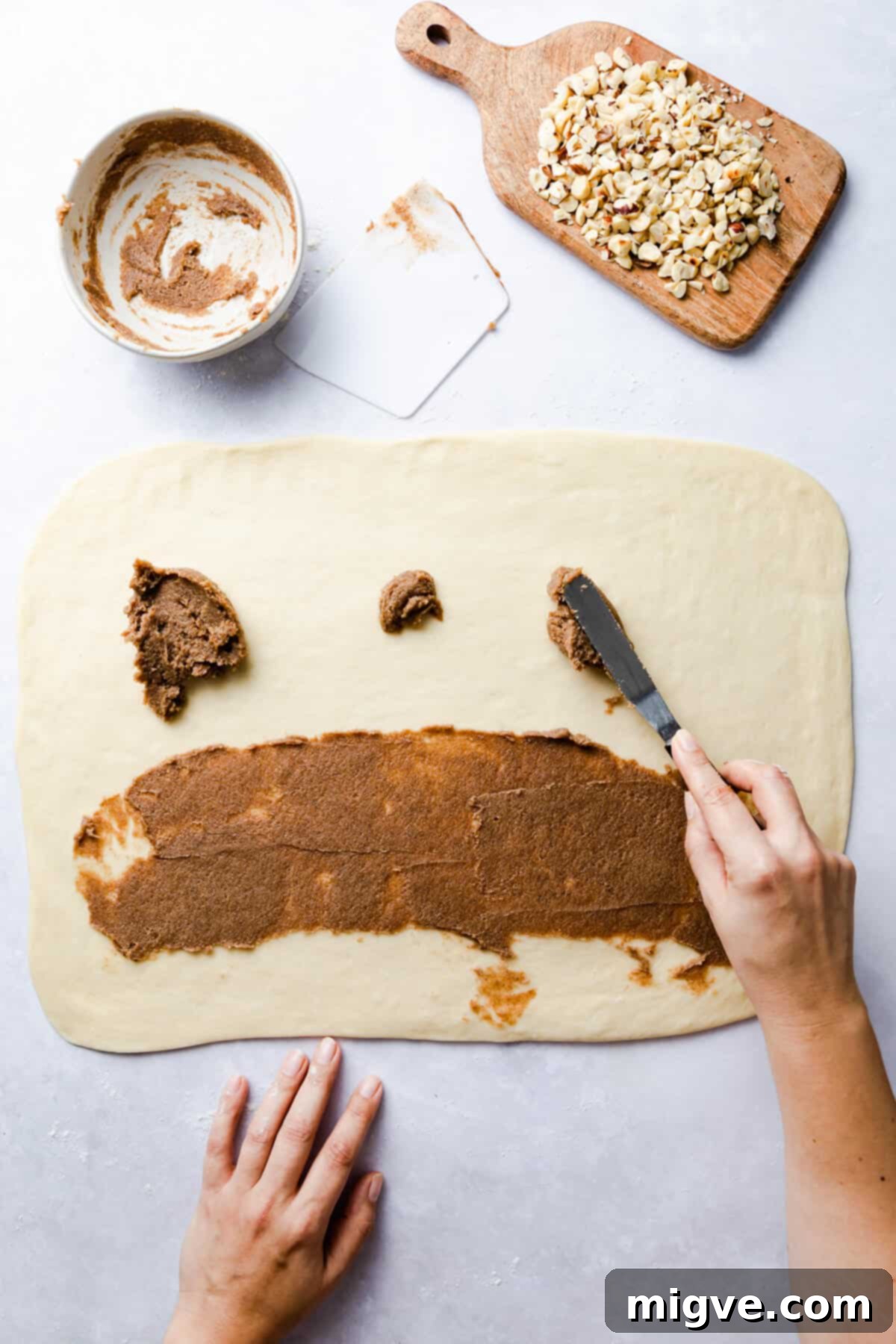 top view of a person spreading cinnamon butter on the surface of dough rectangle