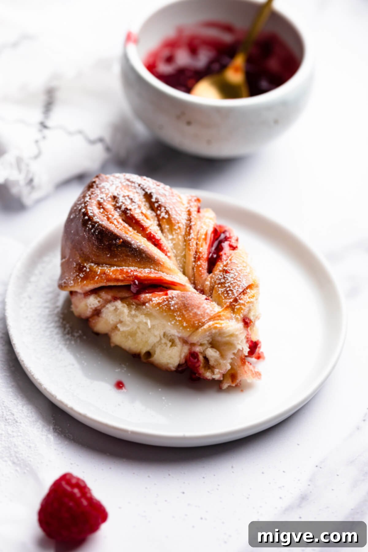45 degree angle view of a piece of star bread with raspberry jam on a small plate