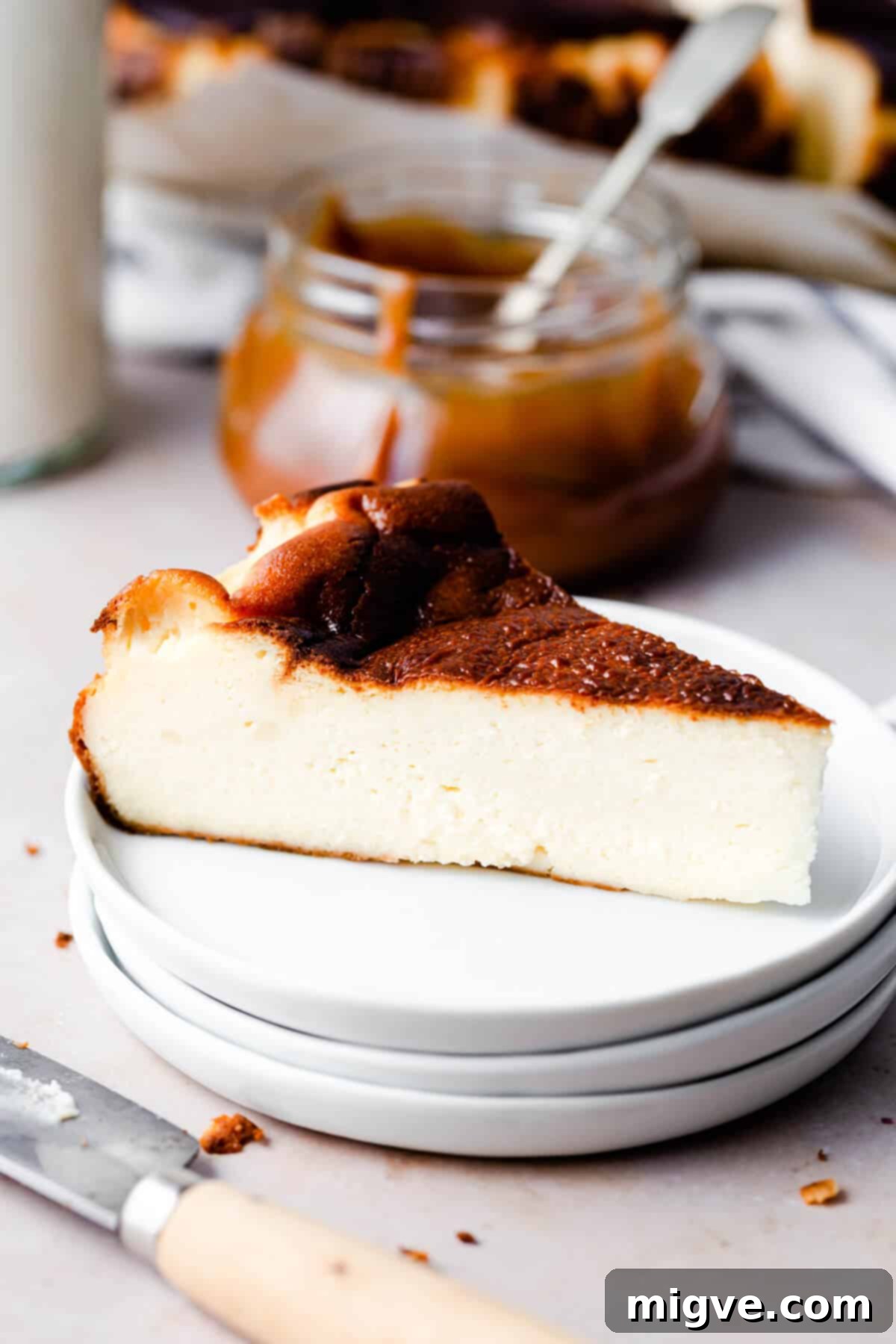 side close up of a slice of cheesecake on a stack of three white plates, ready to be enjoyed.