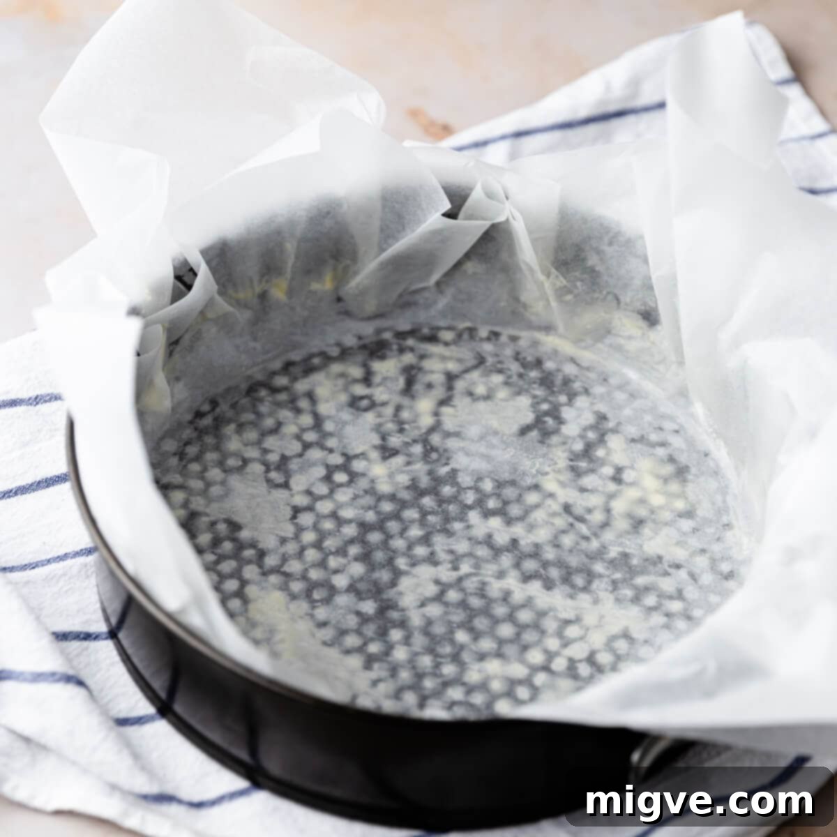 round baking tin lined with baking paper that overhangs, ready for cheesecake batter.